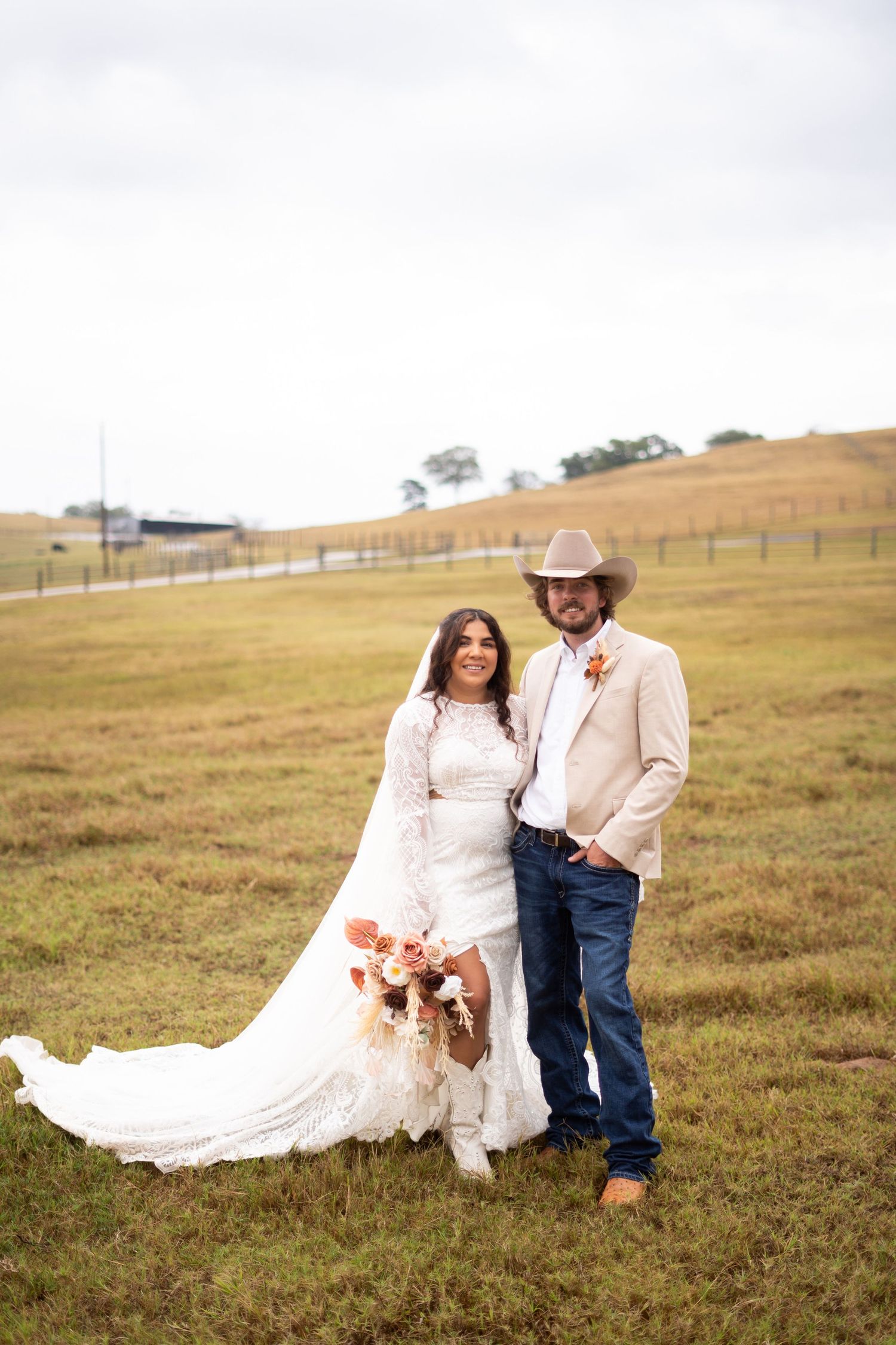 Couple in western wedding attire posing in rolling countryside field.