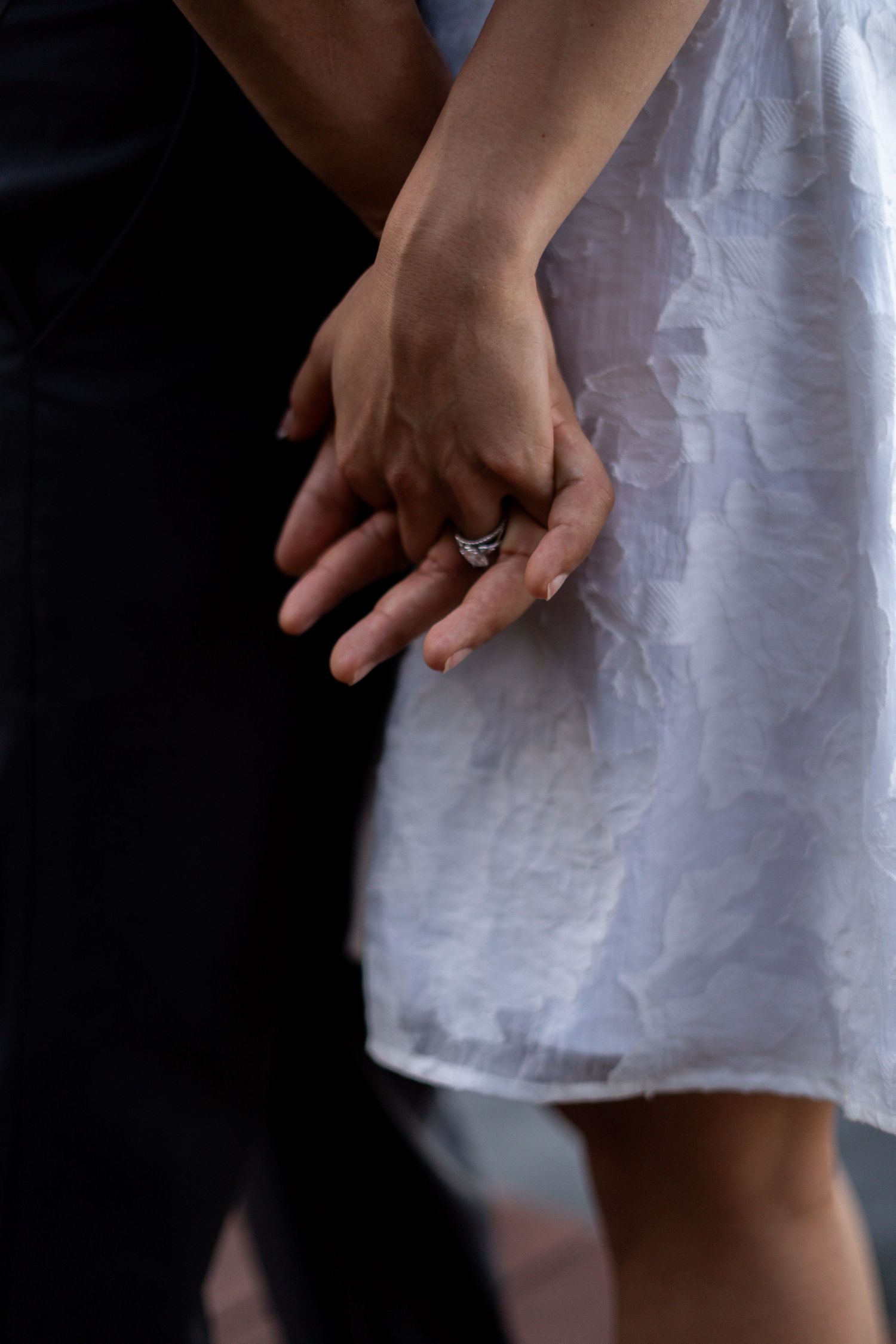 Close-up of hands showing off a new engagement ring against white fabric.
