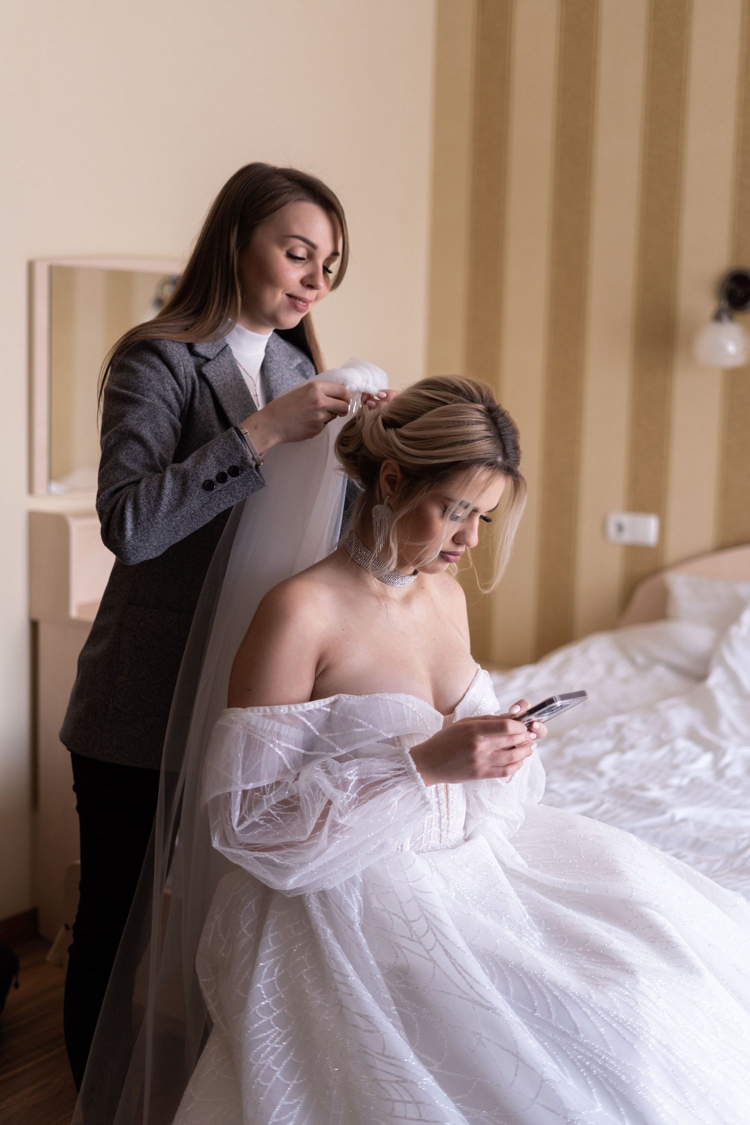 A person helps adjust a flowing white wedding dress on someone preparing for a special occasion.