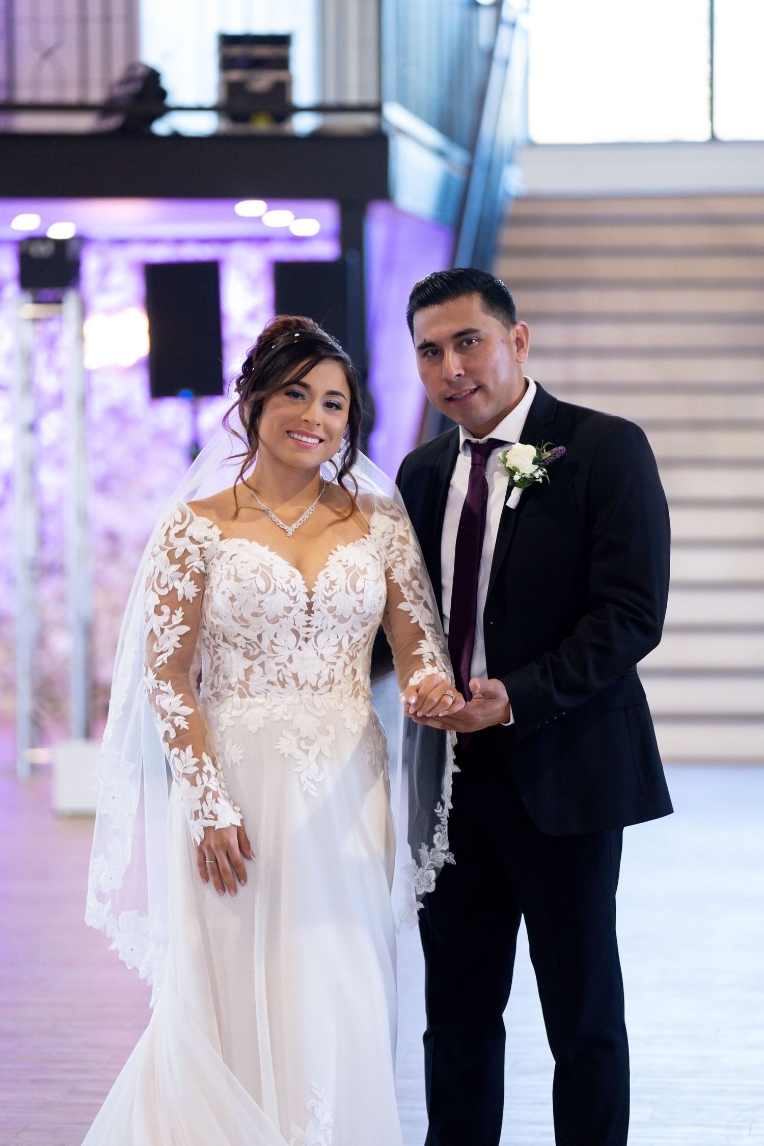 Wedding couple walks together in elegant venue with purple uplighting and white decor.
