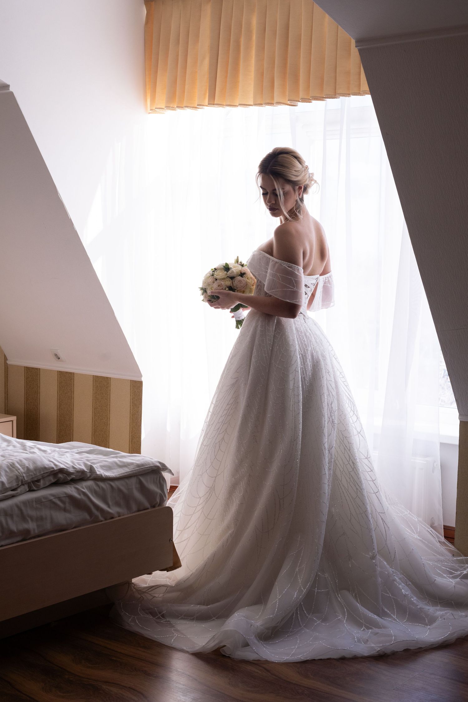A bride in a flowing white wedding gown stands near a window in a series of elegant getting-ready photos.