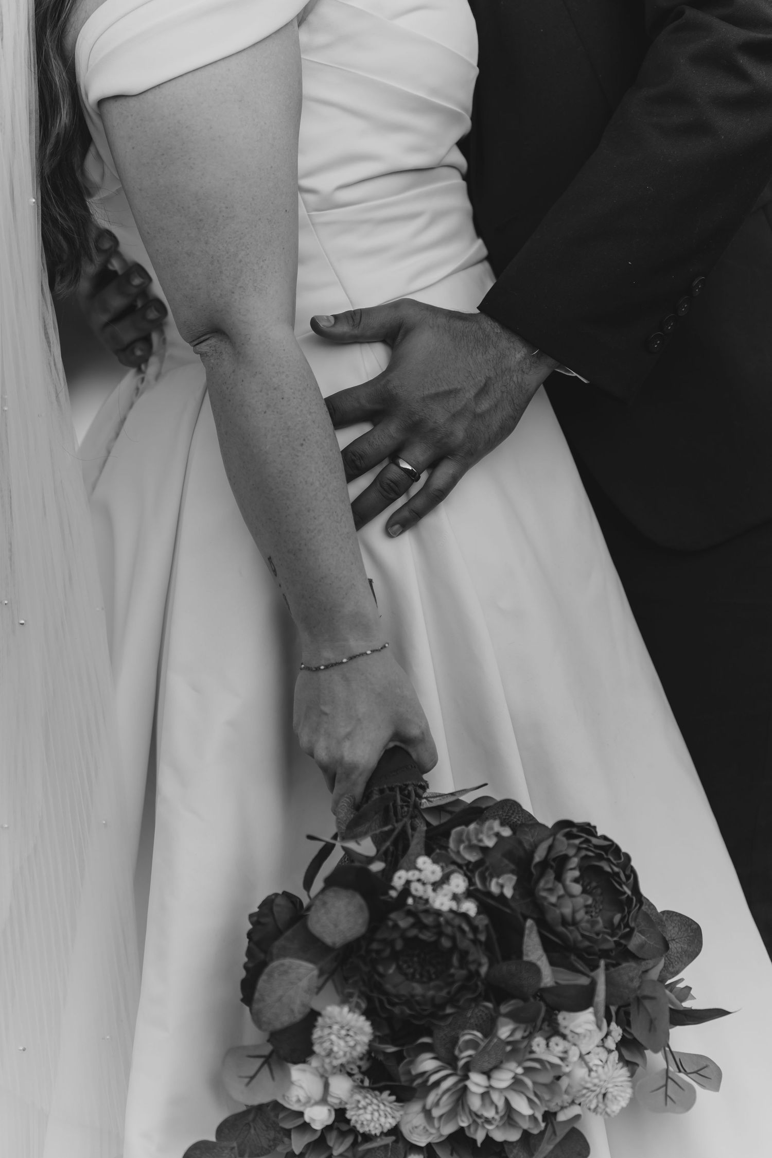 Black and white detail shot of wedding dress and bouquet with dark flowers.