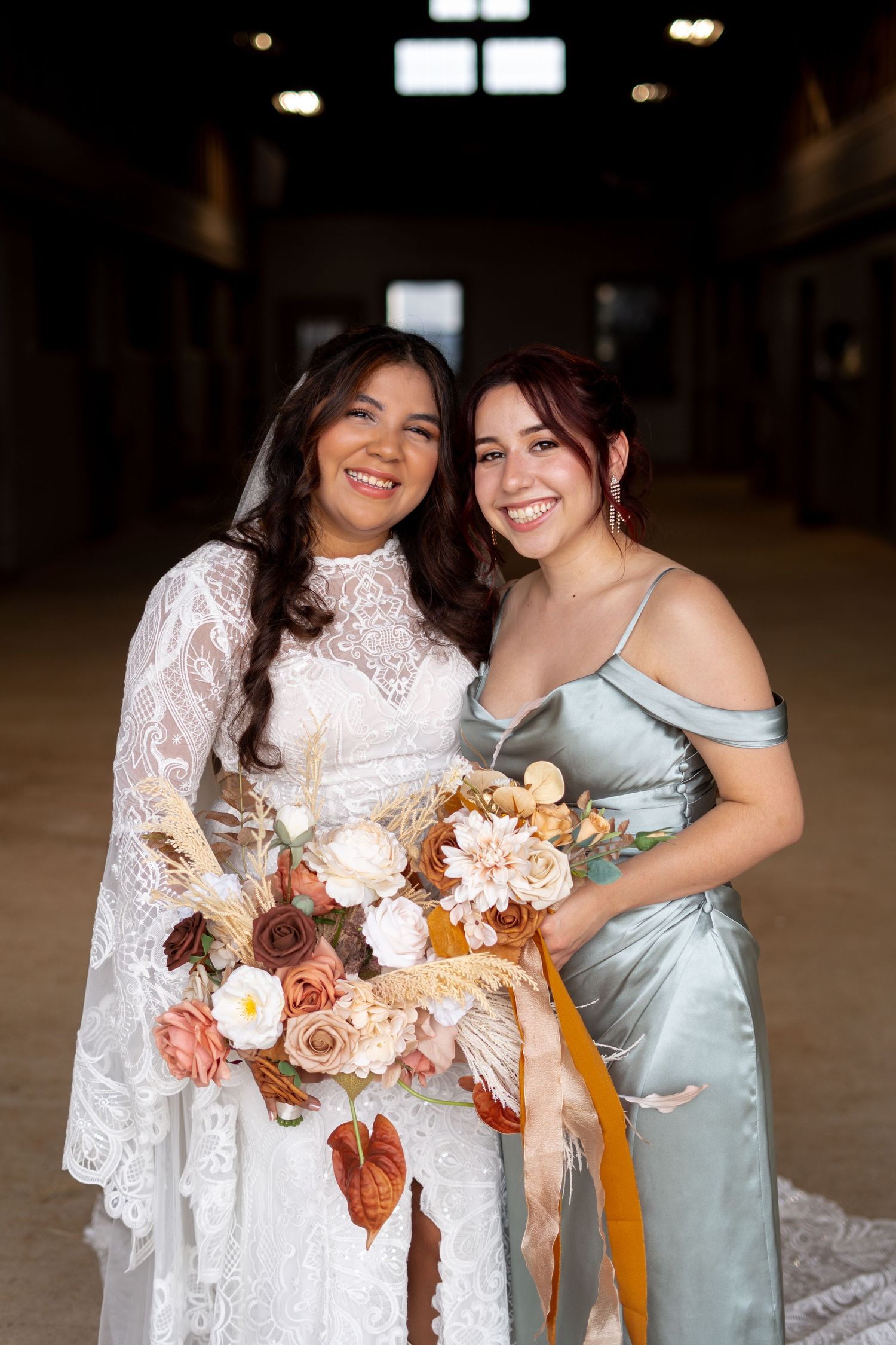A bride and bridesmaid pose together holding a fall-themed wedding bouquet.