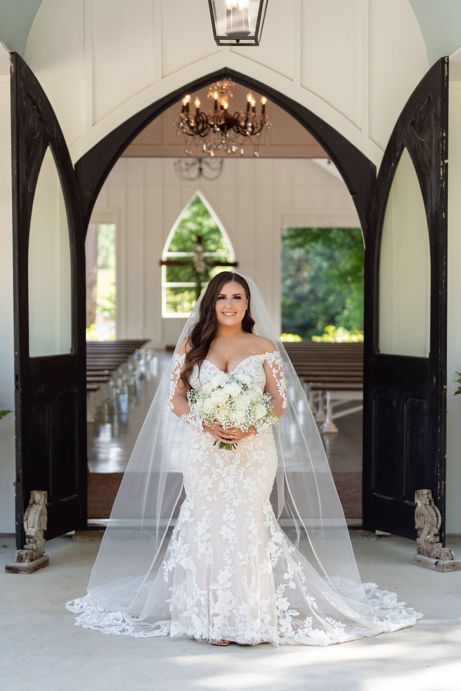 Elegant bridal portraits in white lace wedding dress with long veil captured in a rustic covered walkway with arches.