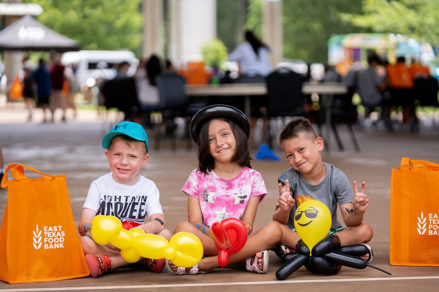 Group of people sitting outdoors with tennis equipment and orange shopping bags.