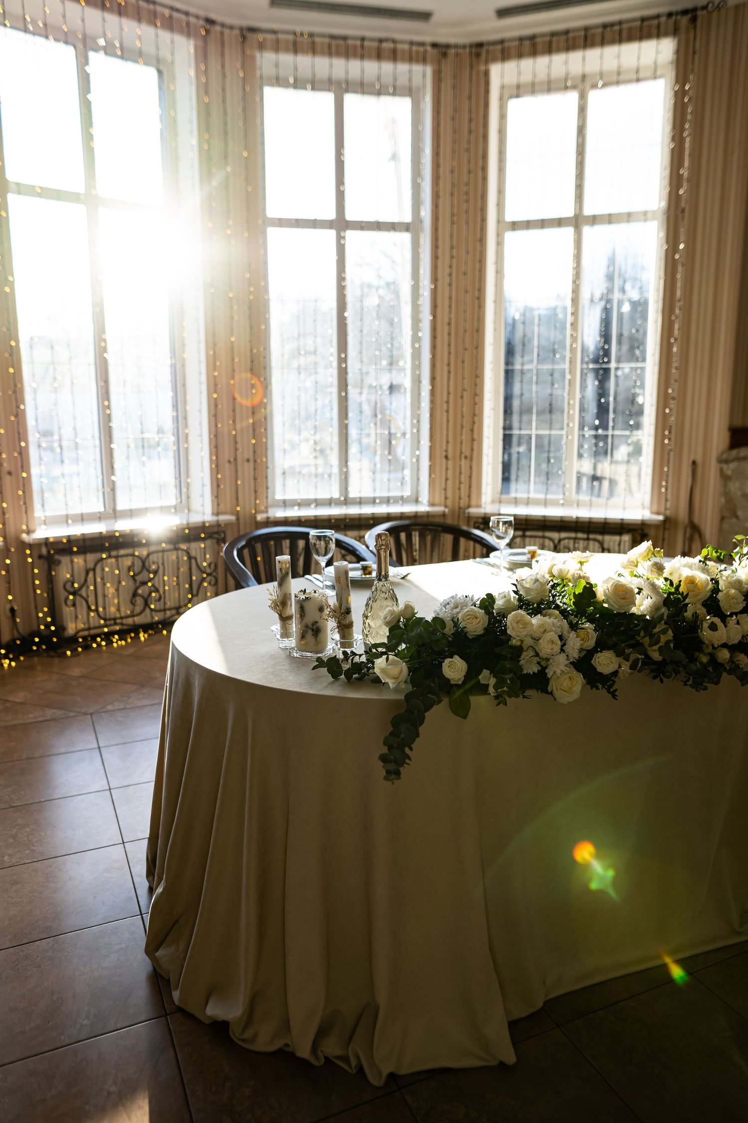 Elegant banquet tables with white linens and floral arrangements line the windows in a bright event space.