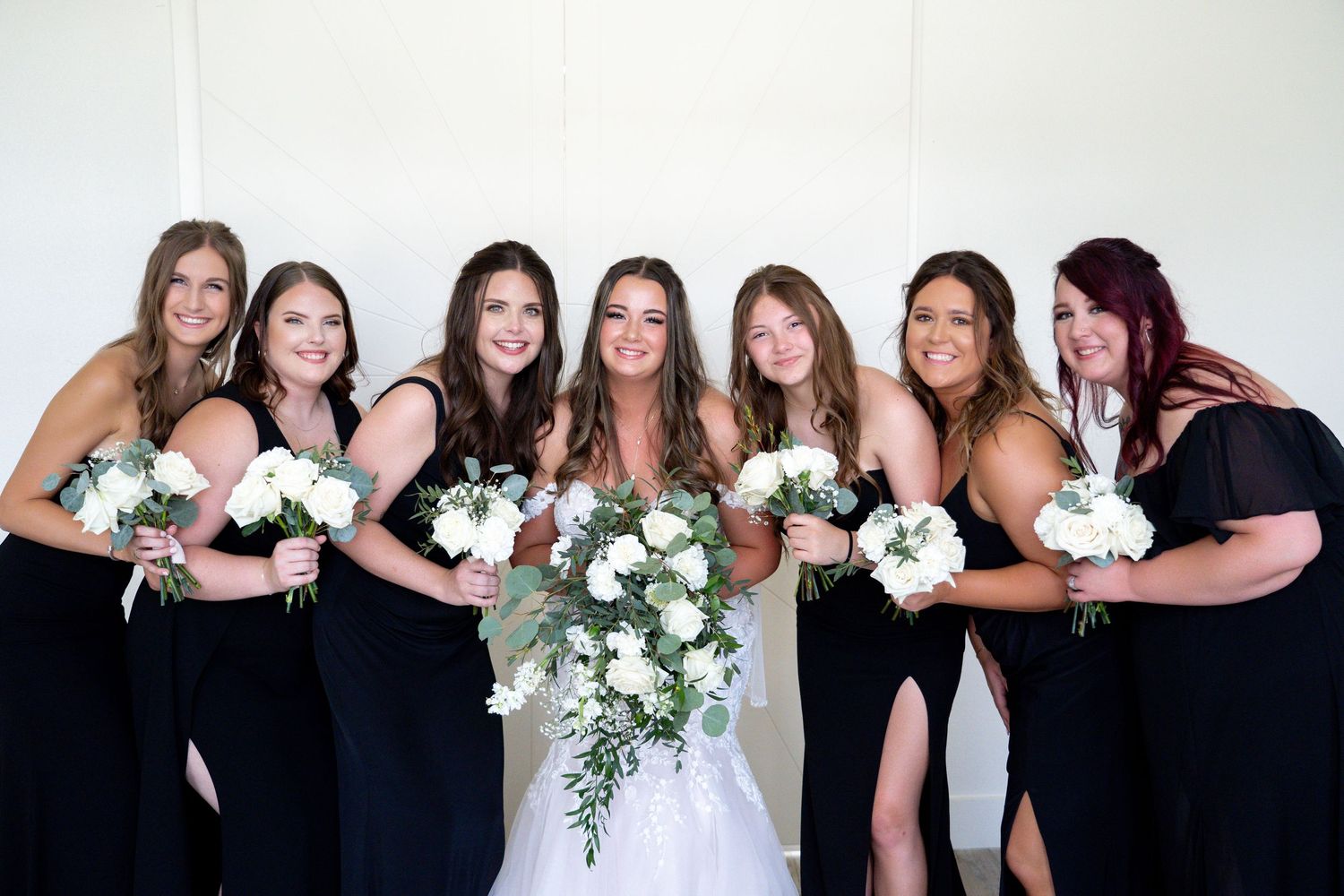 Wedding party wearing black dresses and holding white bouquets pose together in a series of group photos.