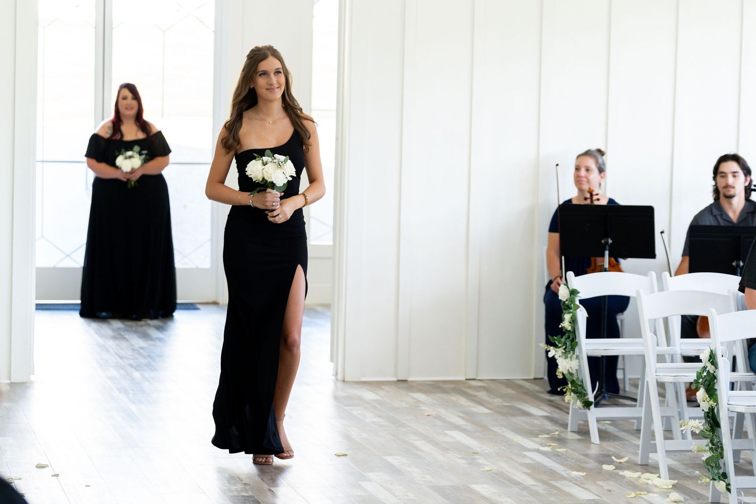 A series of people in black dresses holding white bouquets pose in a bright white studio space for wedding photos.