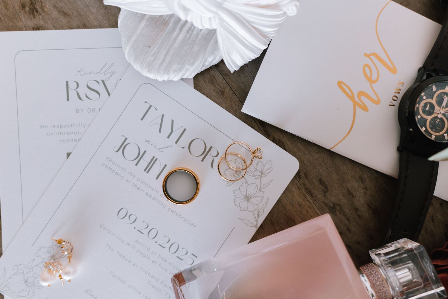 Wedding invitation suite with white and gold calligraphy details displayed on a rustic wooden surface.