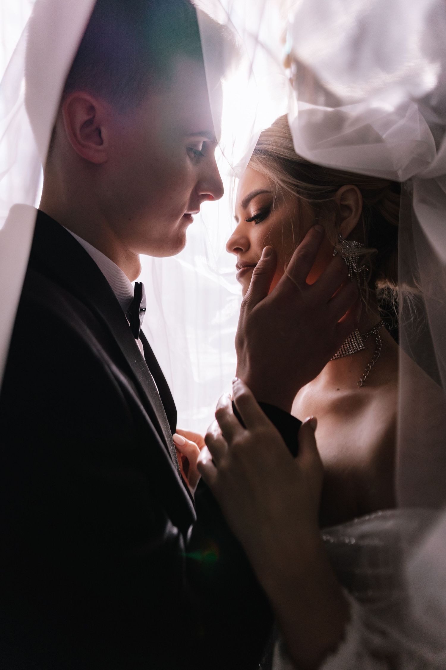 A romantic silhouette of newlyweds sharing an intimate moment under a veil during their wedding ceremony.
