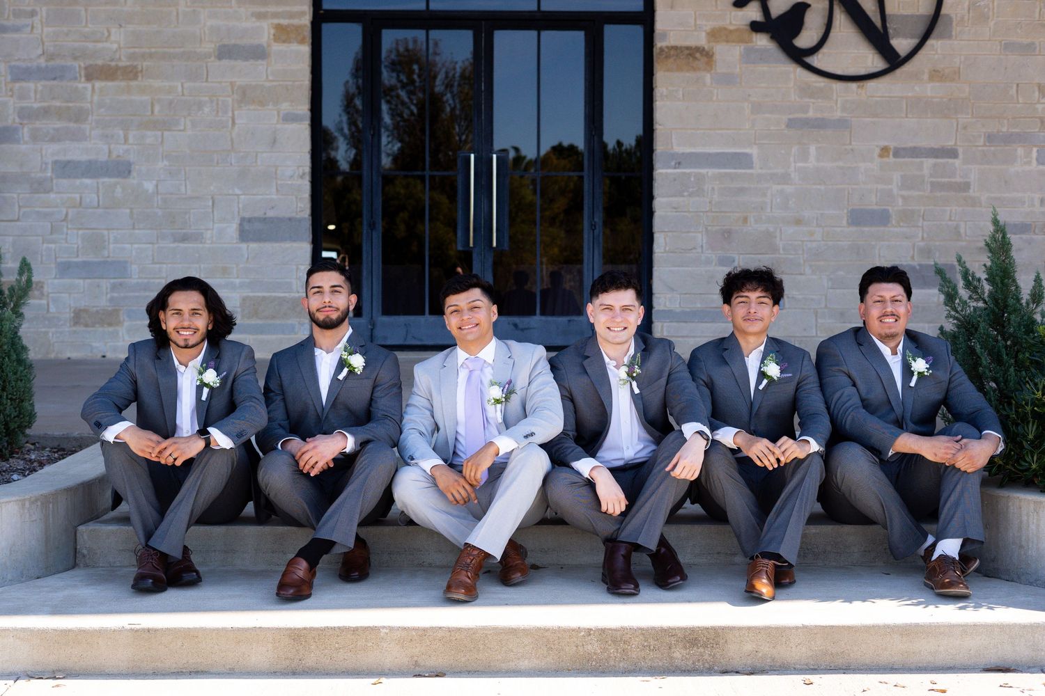 Wedding party members seated casually on stone steps wearing coordinated gray suits.