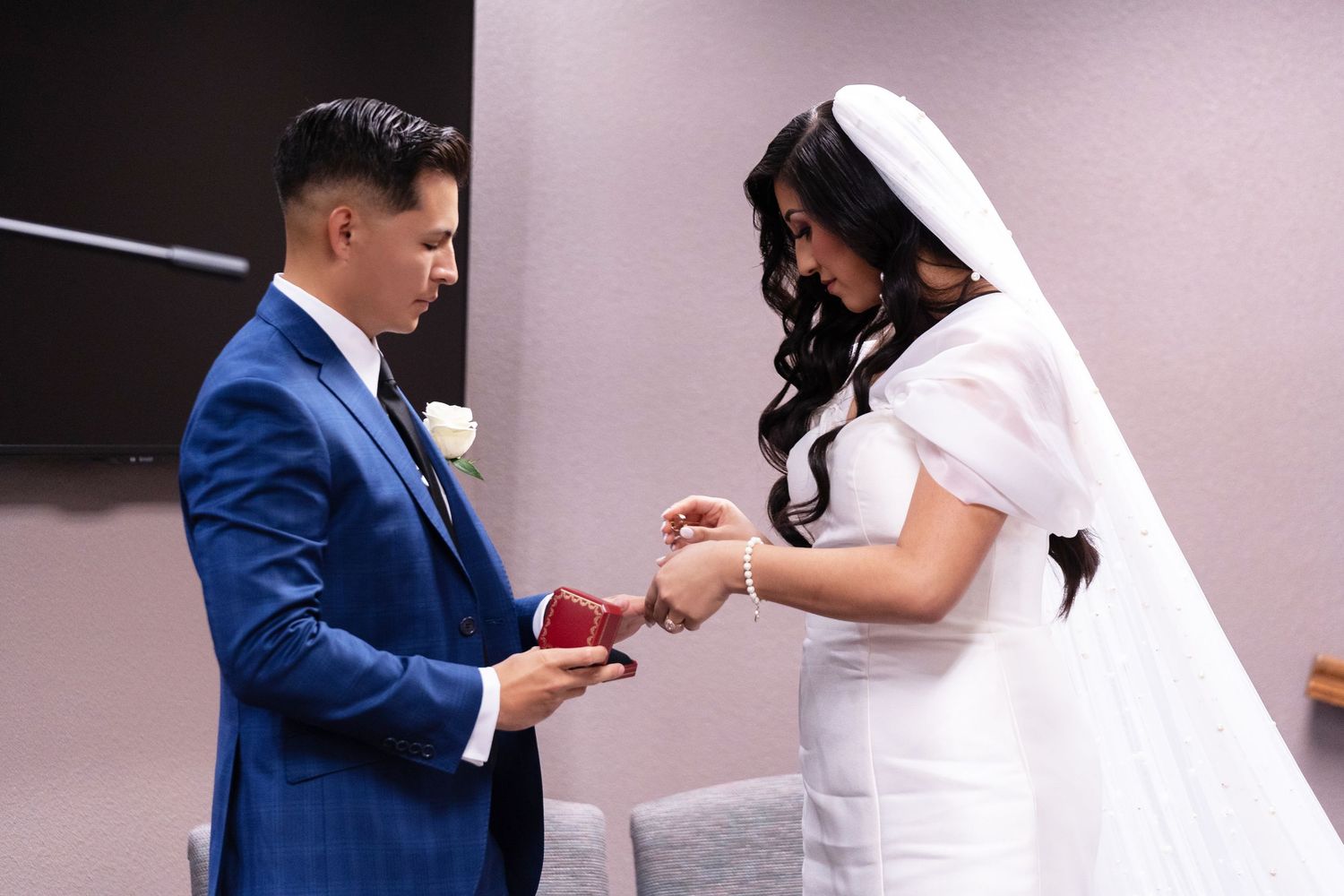 A couple in formal attire during a marriage proposal moment with the person in blue kneeling to present a ring.