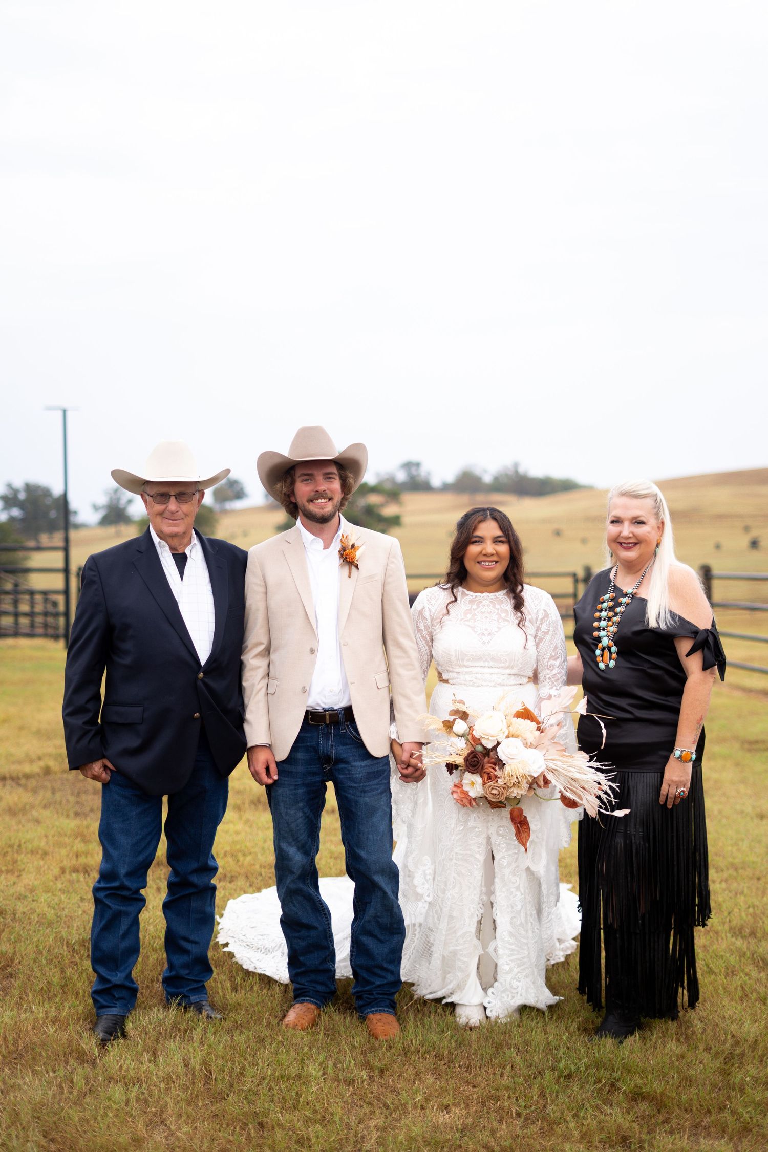 Wedding party in western attire poses together in rustic field setting.
