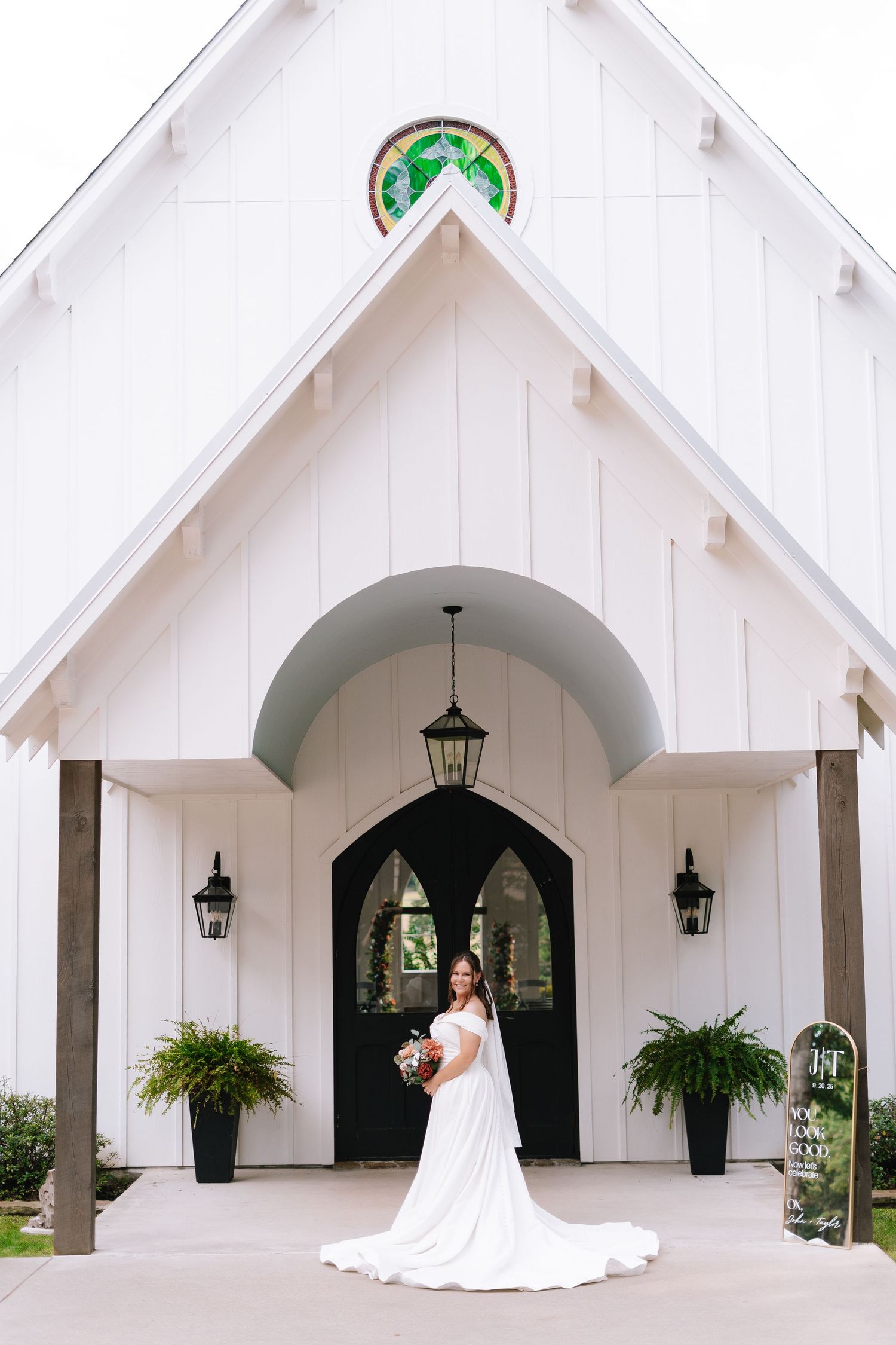 Modern white chapel exterior with Gothic arched doorways and hanging plants creates an elegant wedding venue setting.