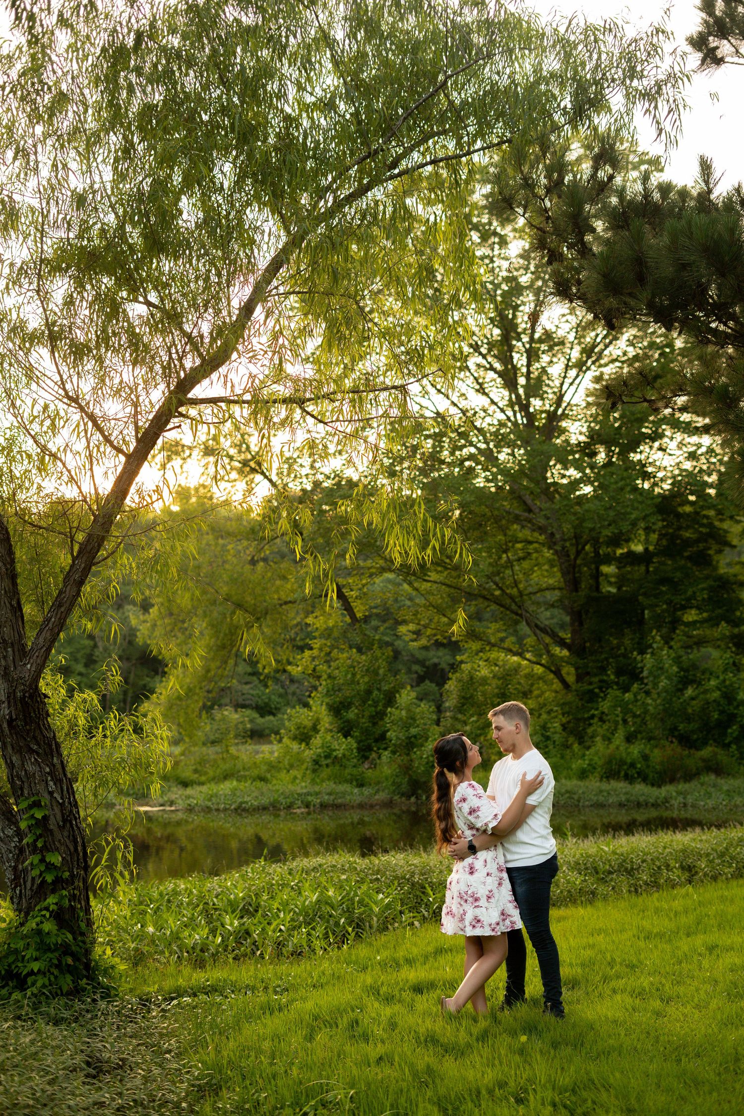 Couple dances and spins in a sunlit meadow surrounded by willow trees at sunset.