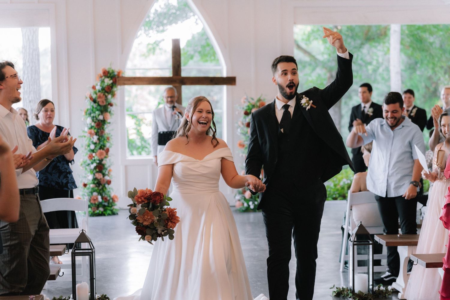 Wedding celebration with guests cheering in chapel decorated with floral arrangements.