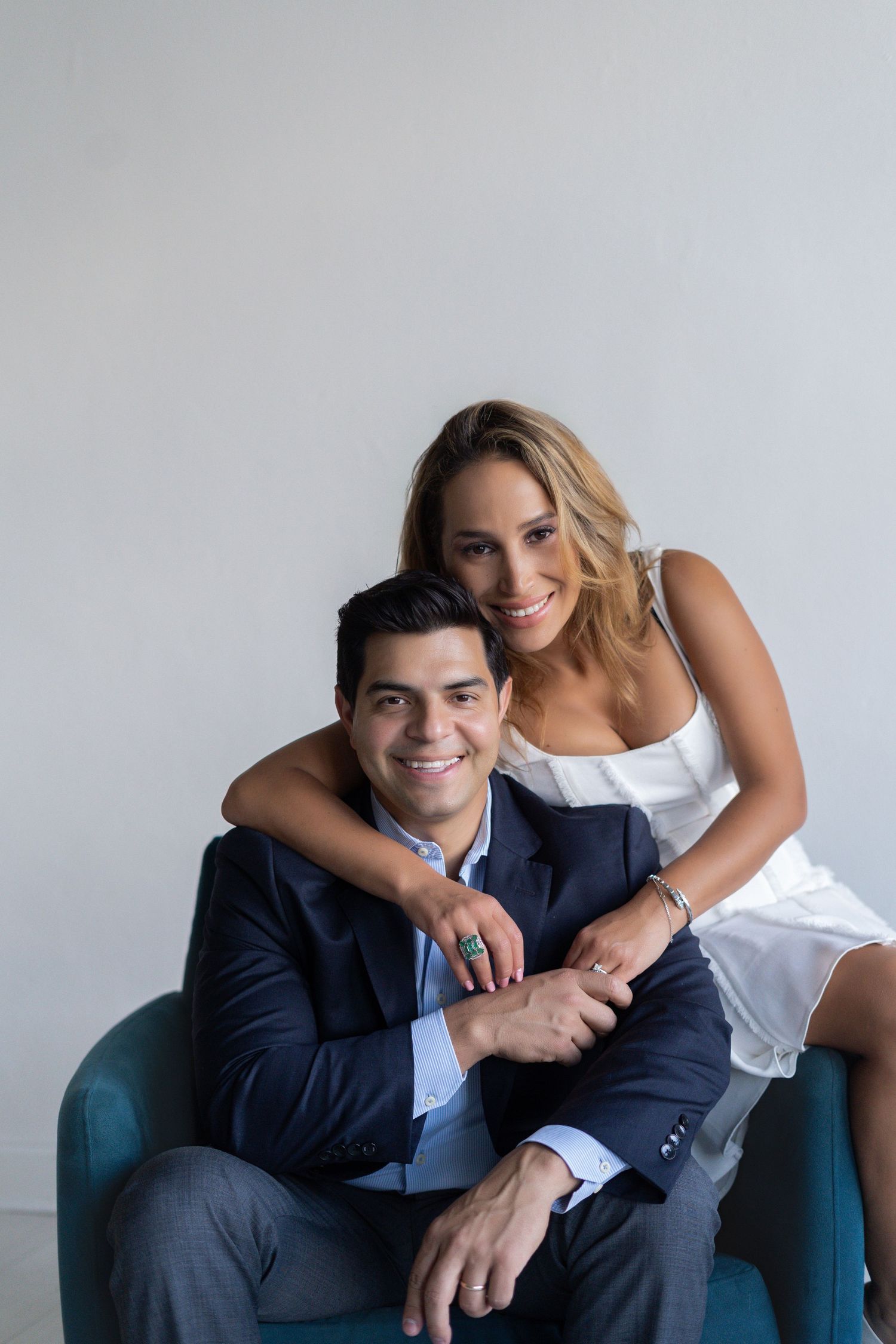 Couple lounges together on a teal chair during an indoor studio photoshoot.
