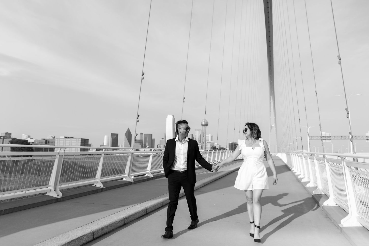 A couple walking along a white bridge in black and white photography.
