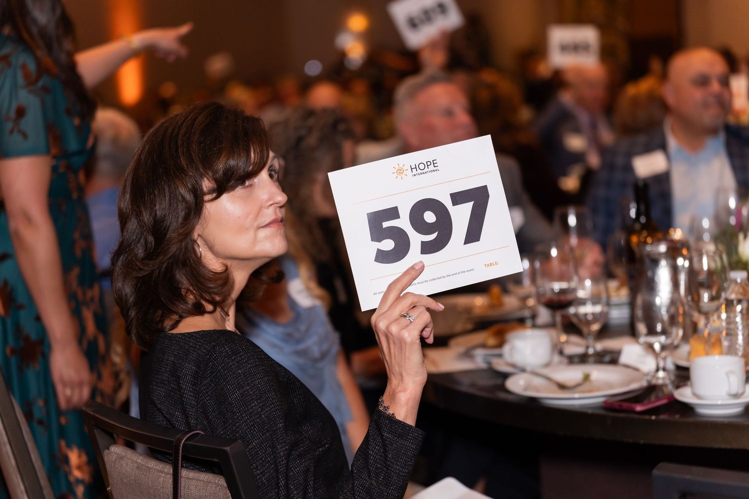 Attendee holding up auction number 597 at fundraising dinner event.