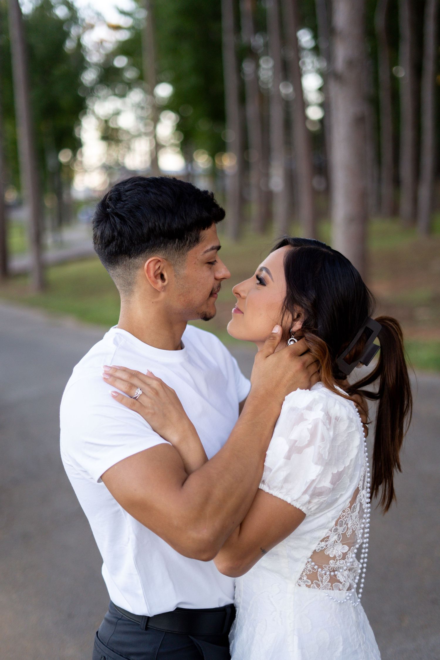 Couple shares romantic moment on tree-lined path in matching white outfits.