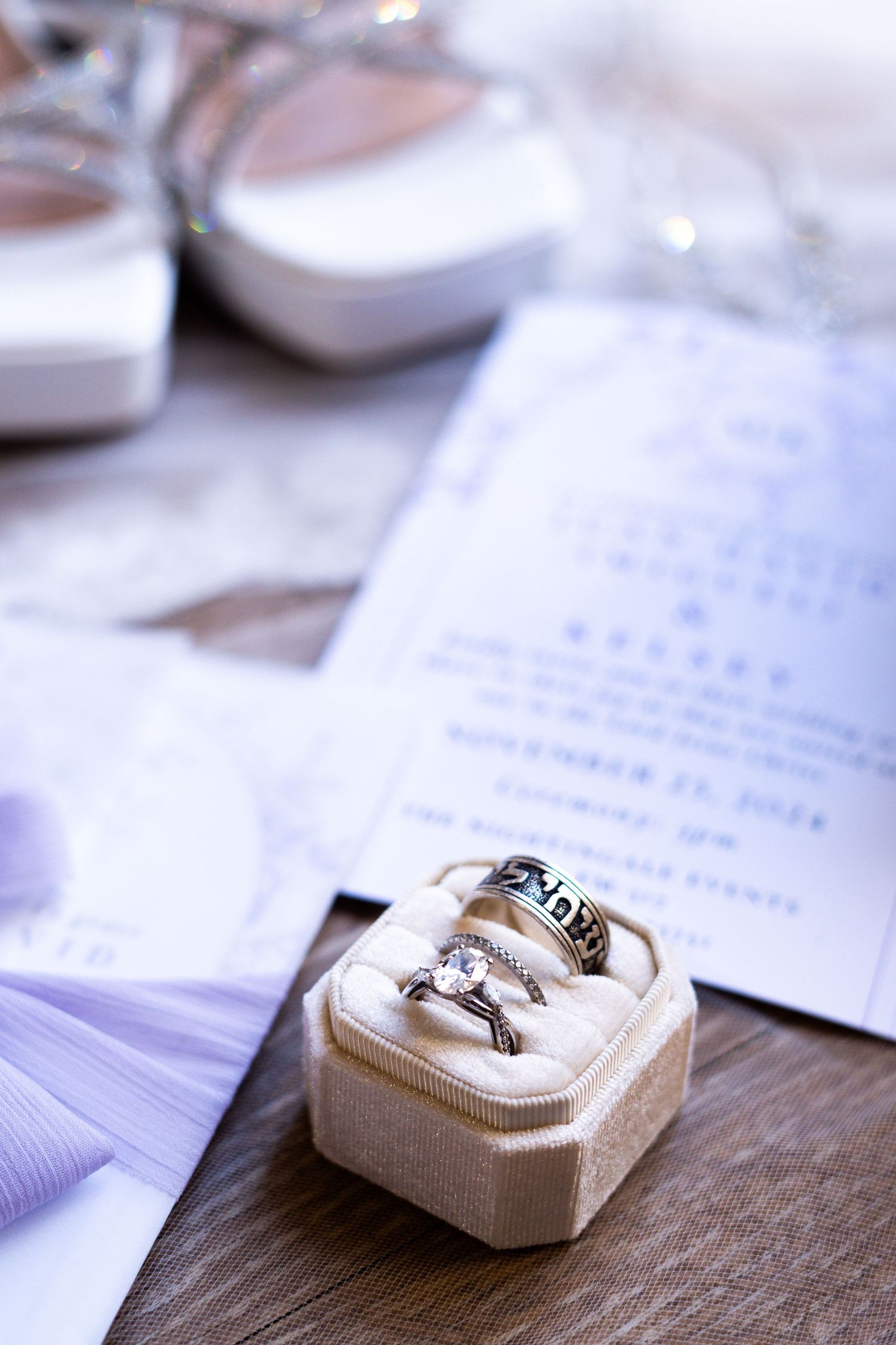 Wedding rings displayed in elegant white ring boxes on a wooden surface with invitation cards.