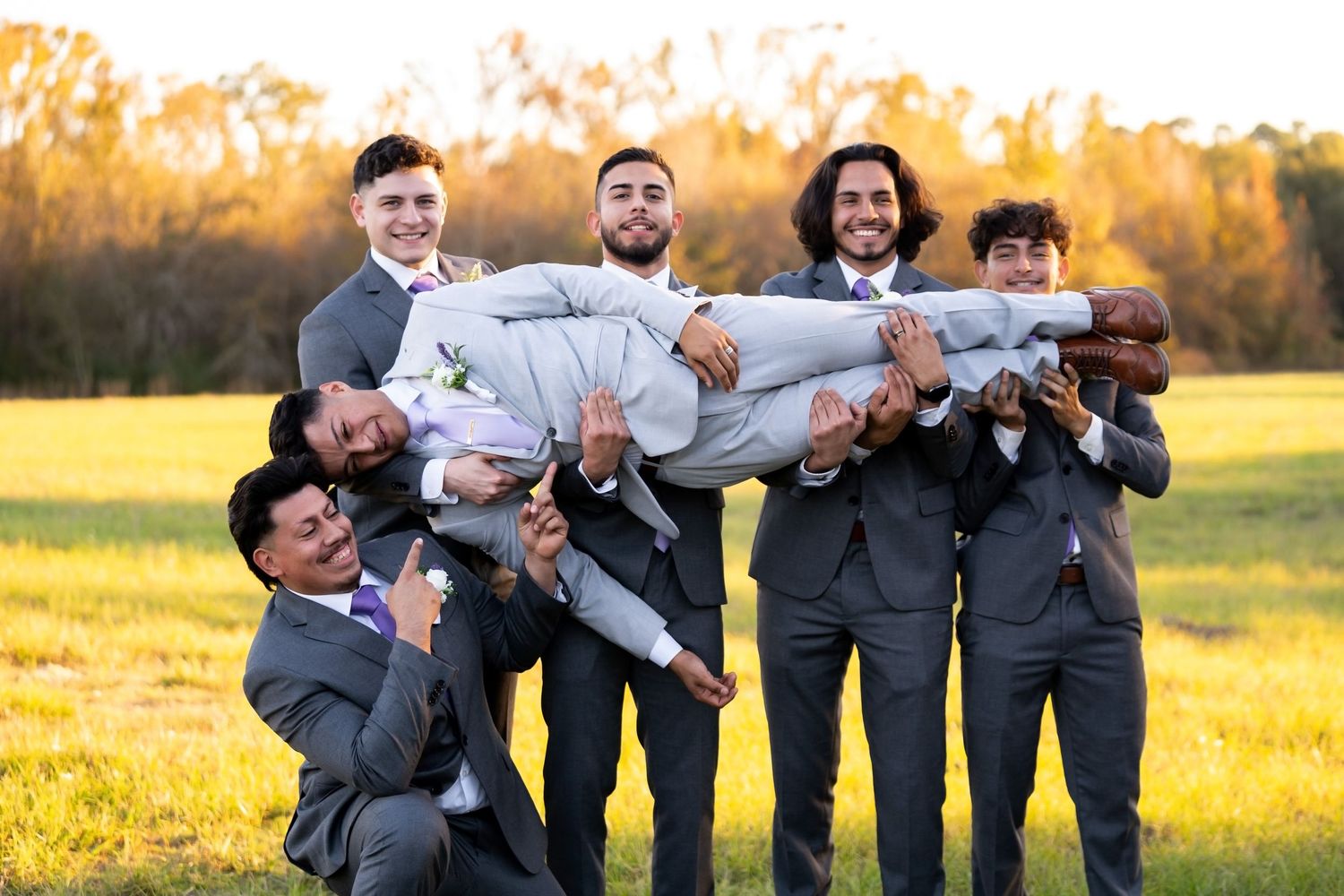Wedding party members in gray suits strike fun poses during sunset photo session.