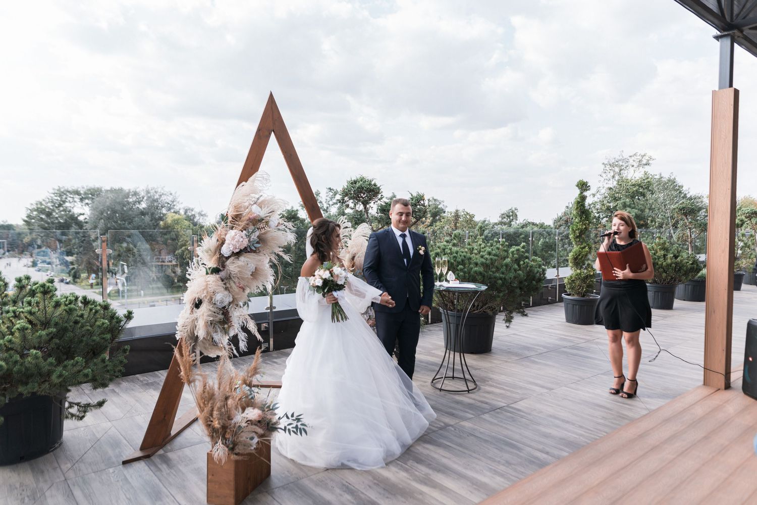 A romantic wedding couple poses on a beachfront deck with ocean views and tropical greenery in the background.