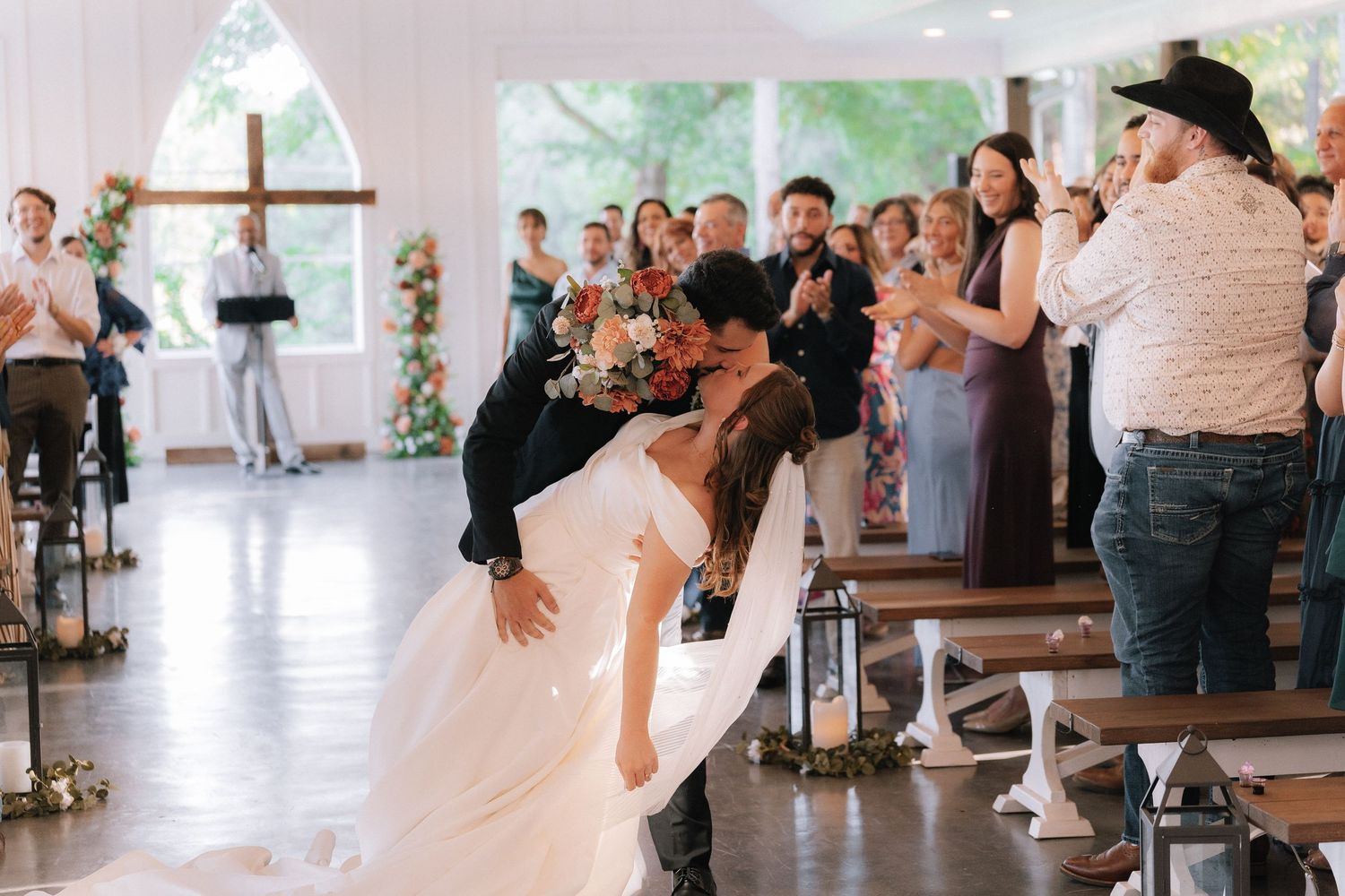 Wedding guests watching ceremony from white chairs in an elegant venue.
