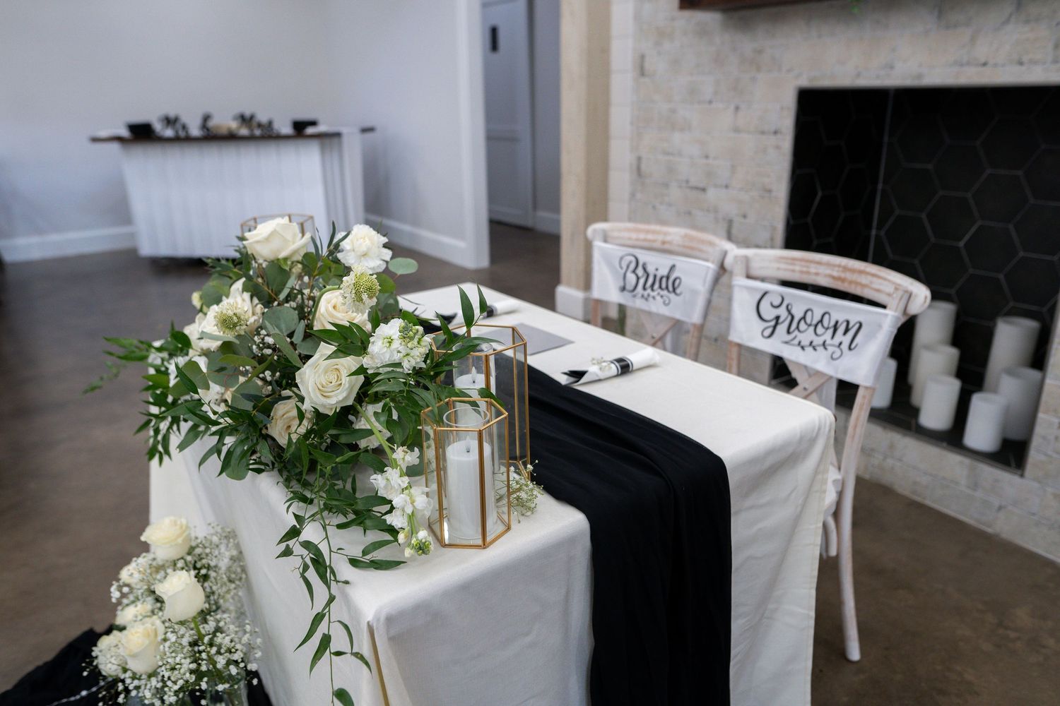 Elegant white floral wedding centerpieces with greenery and gold accents arranged on rustic wooden tables.