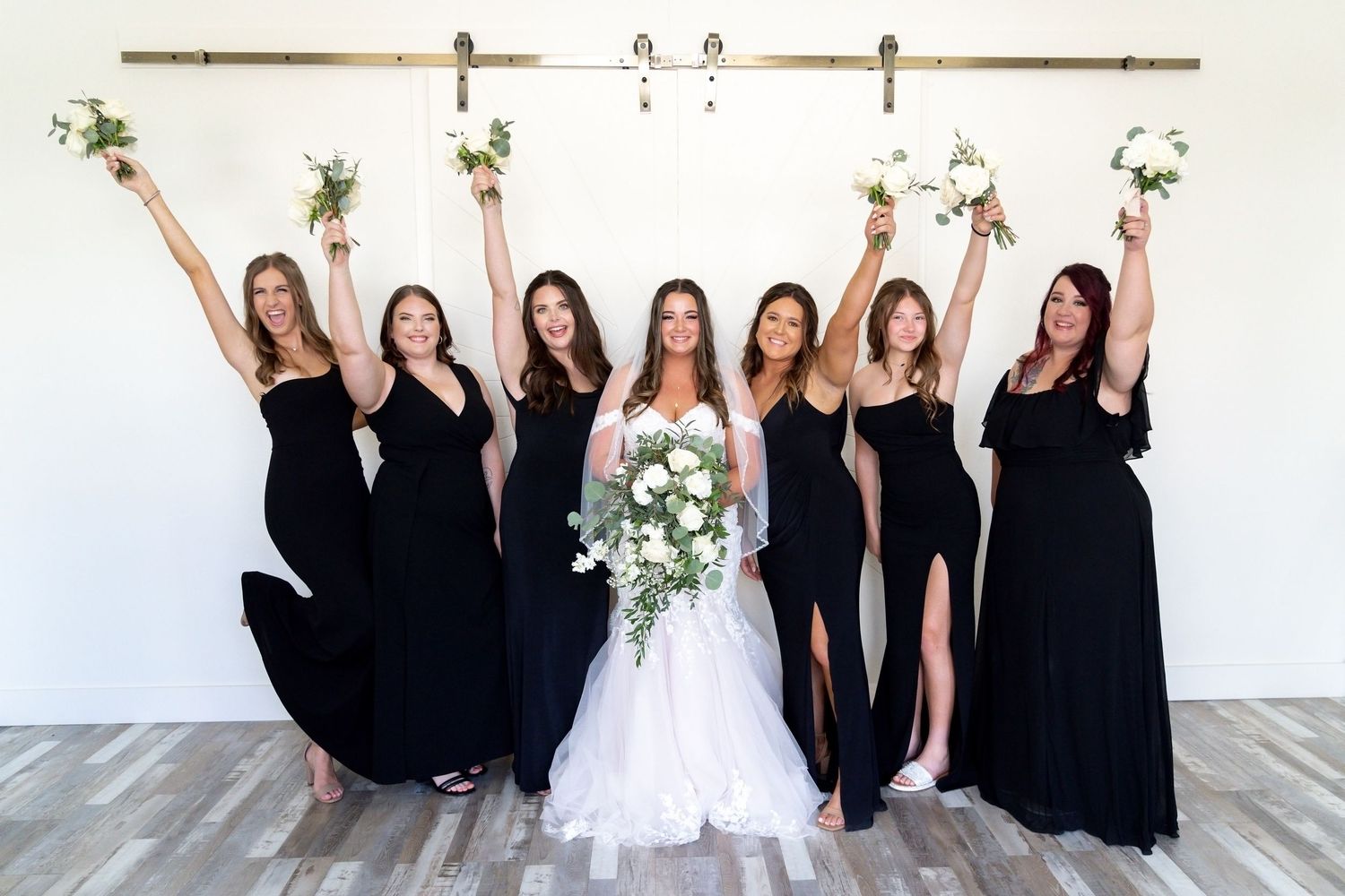 A wedding party poses together with bridesmaids in black dresses and the bride in a white gown.
