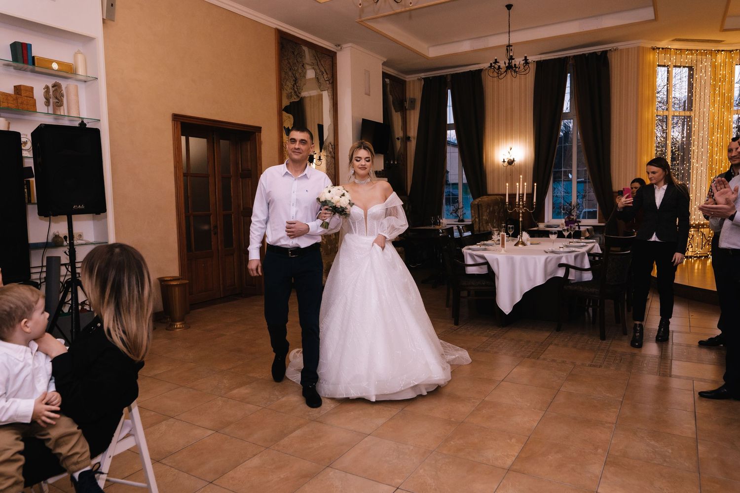 Wedding guests dance and celebrate in an elegant ballroom with chandeliers and warm lighting during a reception.