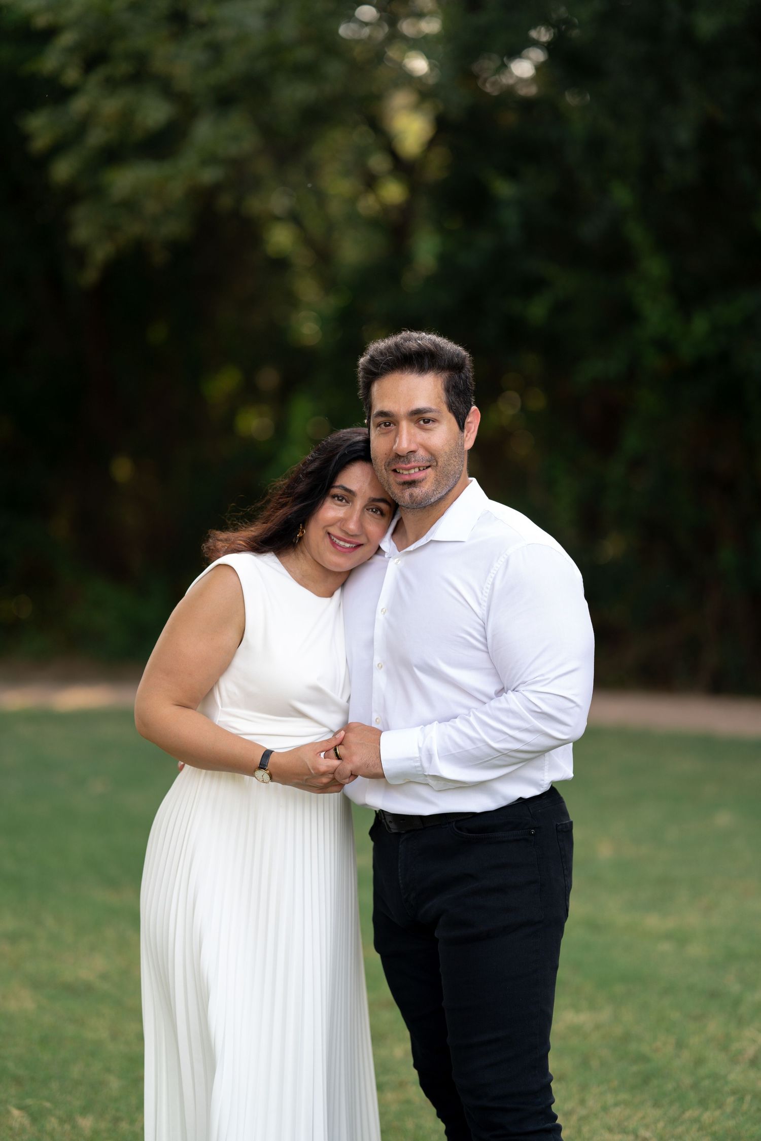 Couple in white outfits sharing tender moments in an outdoor garden setting.