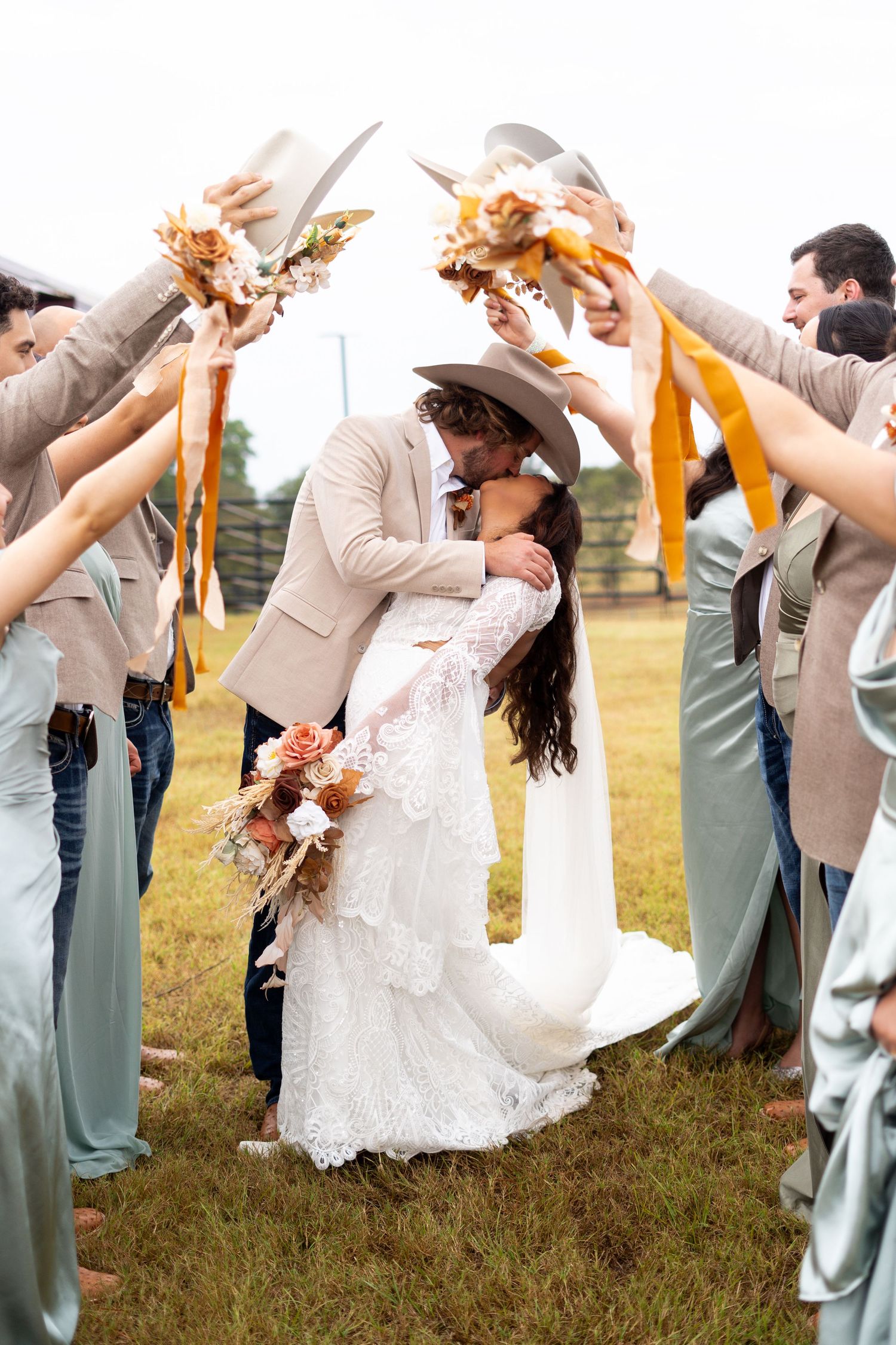 A wedding party holds bouquets overhead while the couple shares a romantic moment.