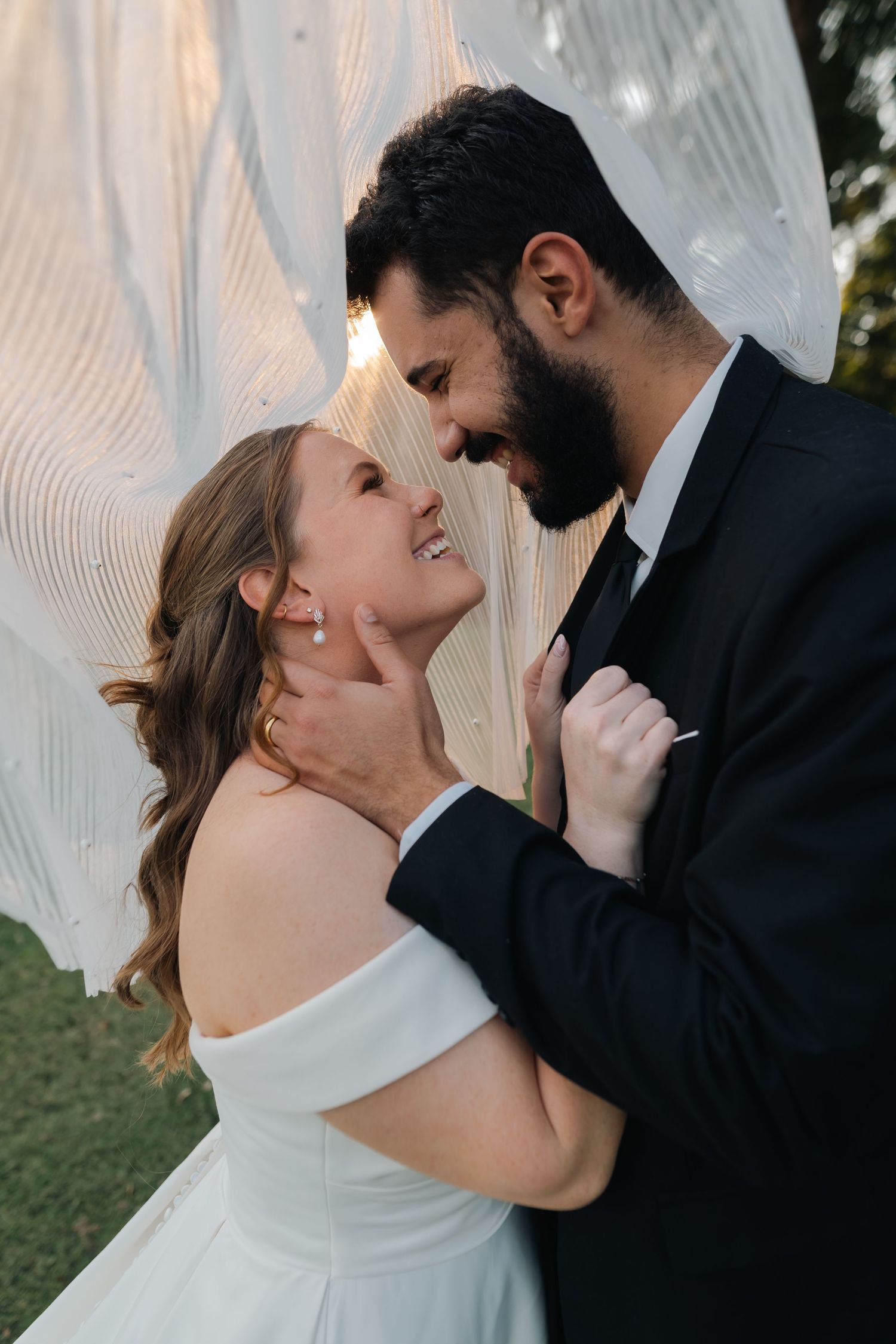 An intimate wedding moment captured with a flowing veil backdrop in an outdoor setting.
