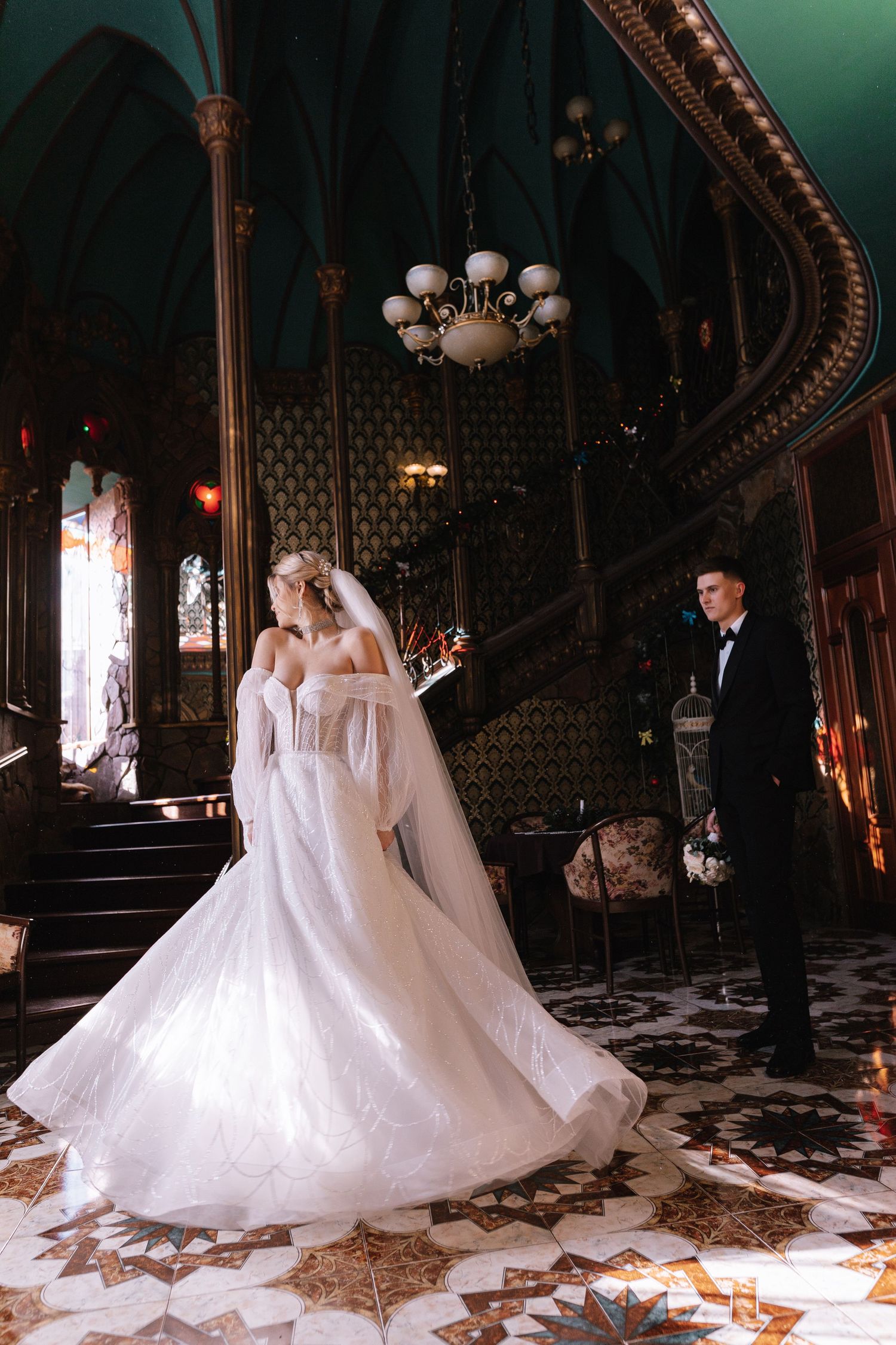 A wedding couple twirls gracefully across an ornate Victorian-style ballroom with patterned floors and vintage decor.