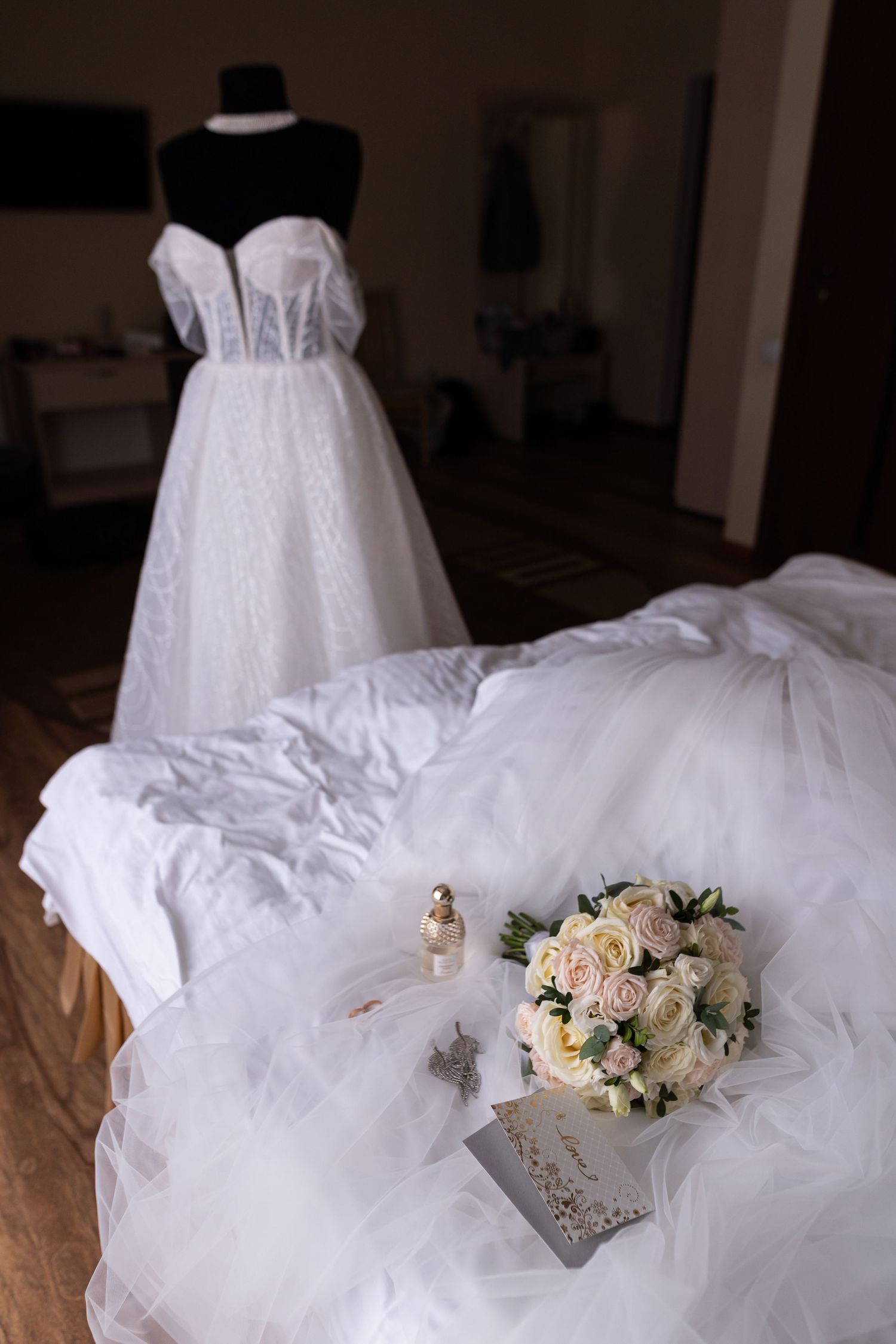 Elegant white wedding dress with tulle skirt and delicate floral bouquet in peach and cream tones laid against fabric.