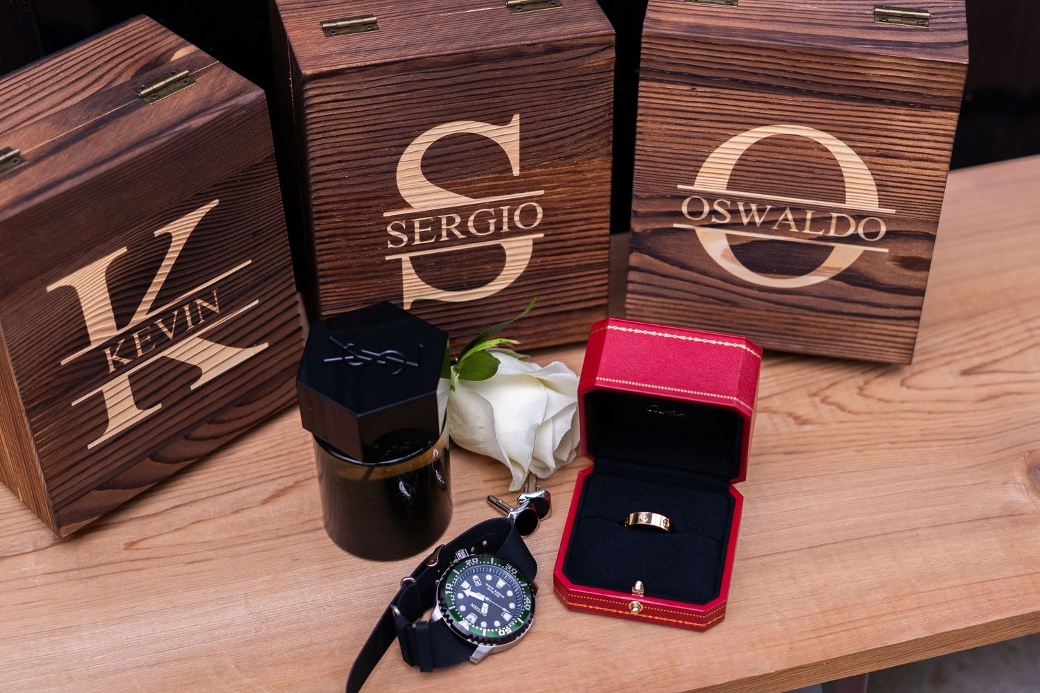 Custom engraved wooden gift boxes with monograms displayed alongside jewelry and watches on a wooden surface.
