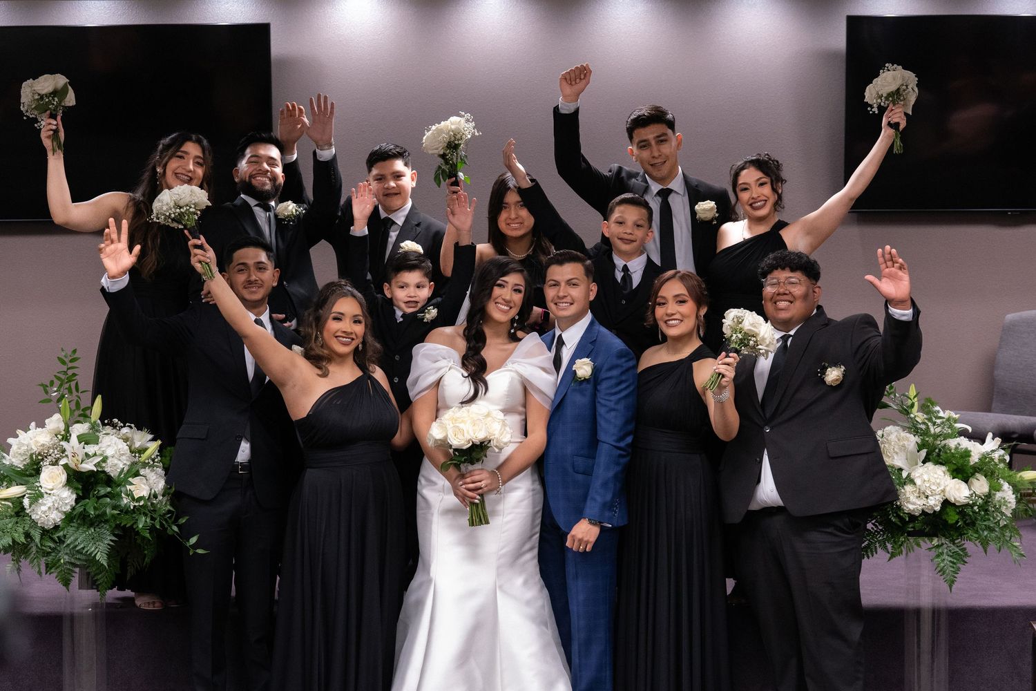 Wedding party members raise their hands in celebration during a joyful reception moment.