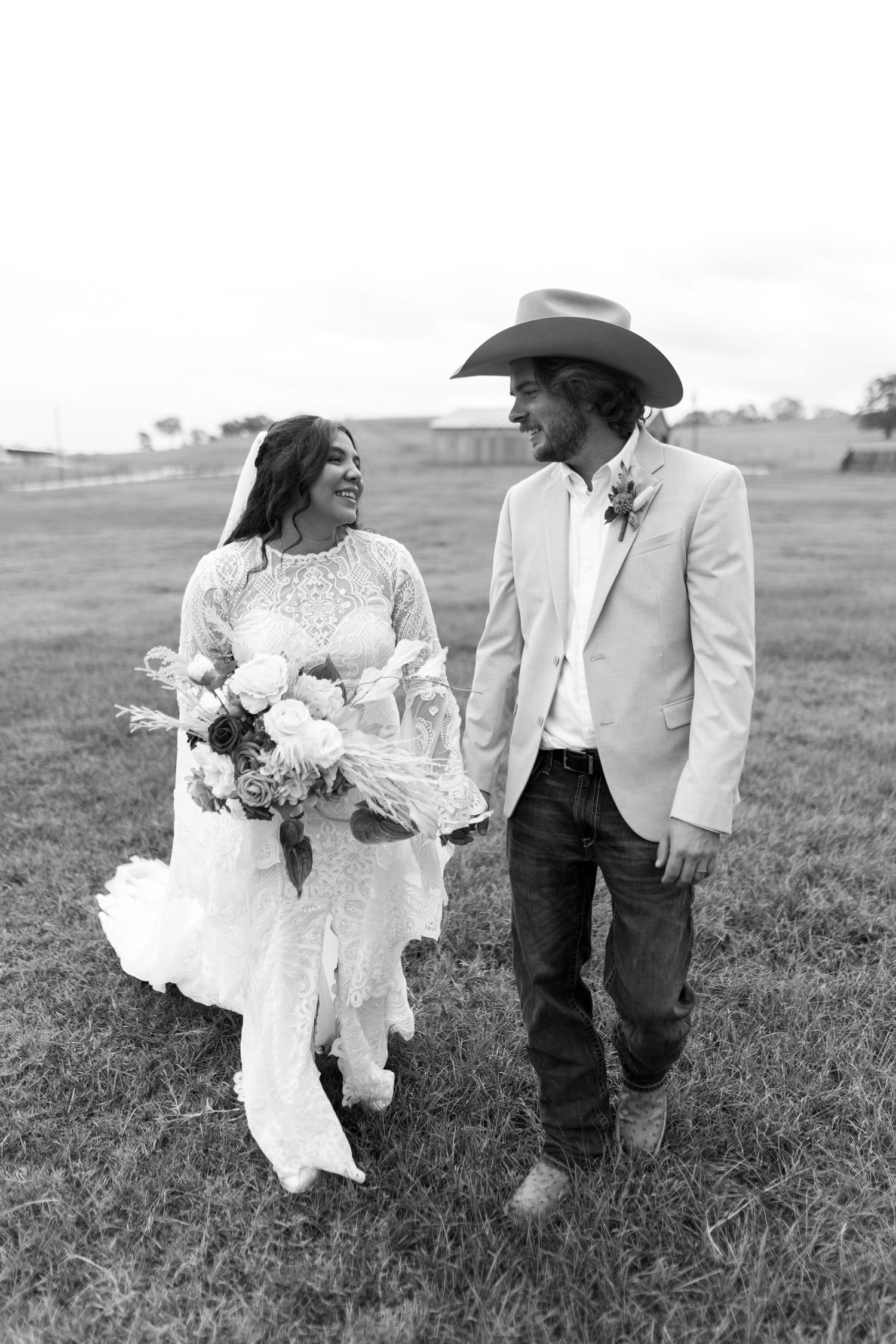 A black and white photo of a couple walking and laughing together in wedding attire on a grassy field.
