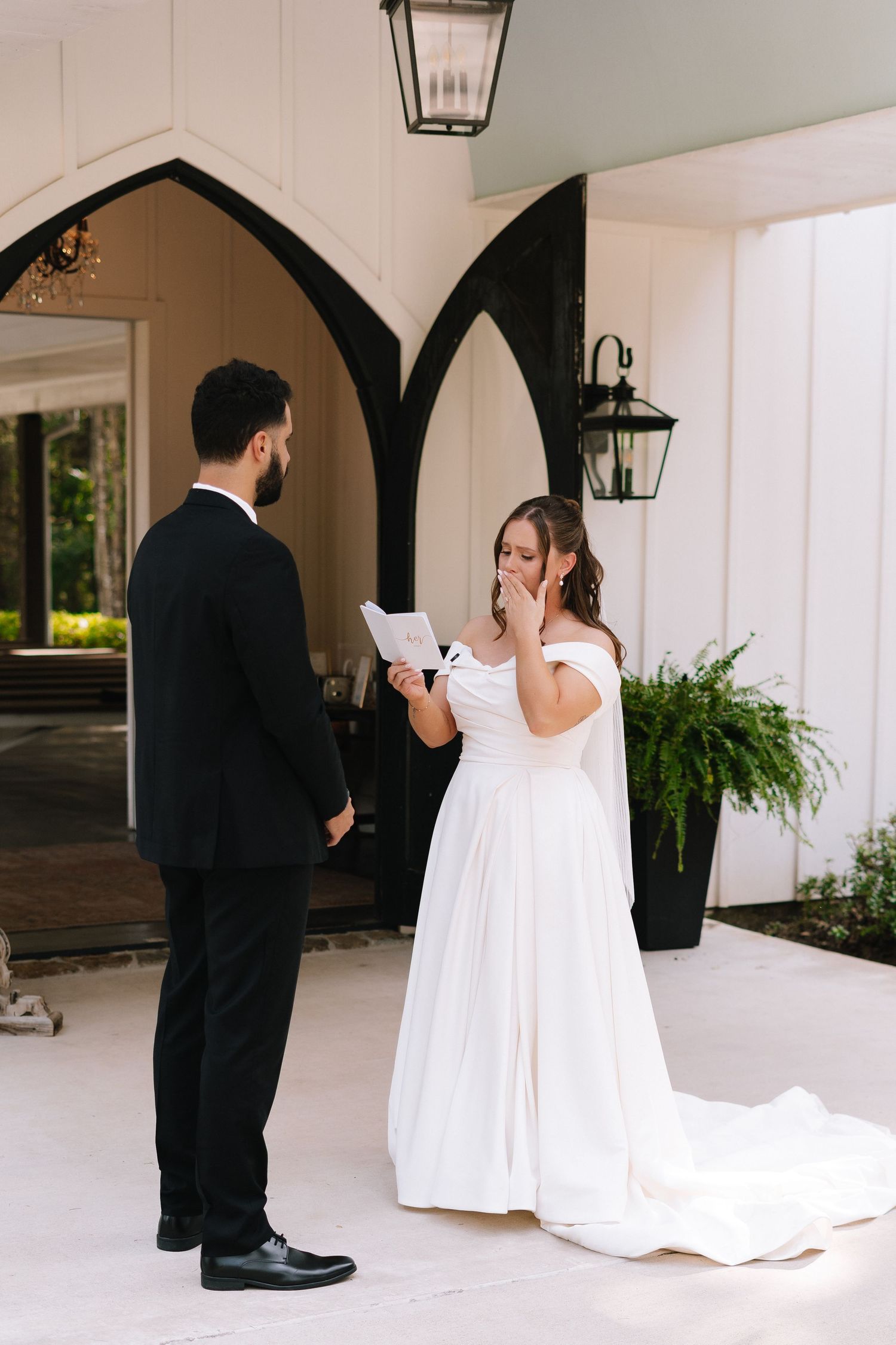 A couple shares an emotional moment during their wedding ceremony under elegant arched walkways.