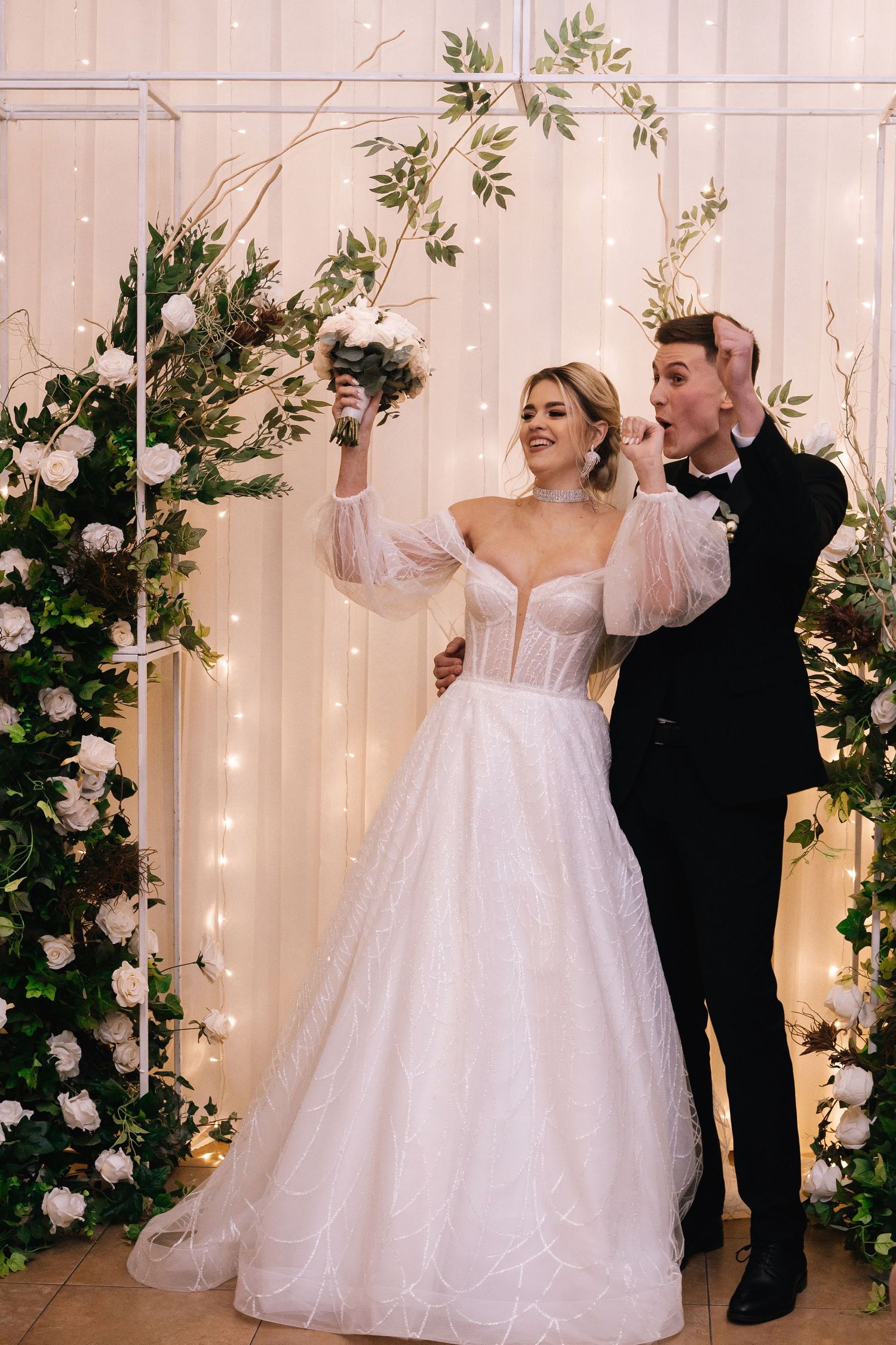 A couple dancing and twirling together in a romantic setting with white twinkle lights and floral decorations.