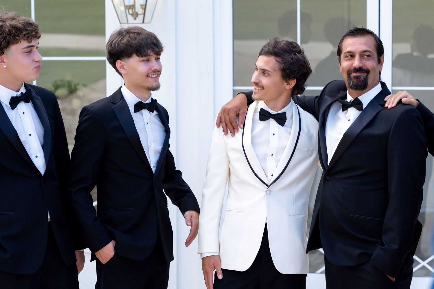 A group in formal attire including black tuxedos and white jackets pose together for a formal event photo.