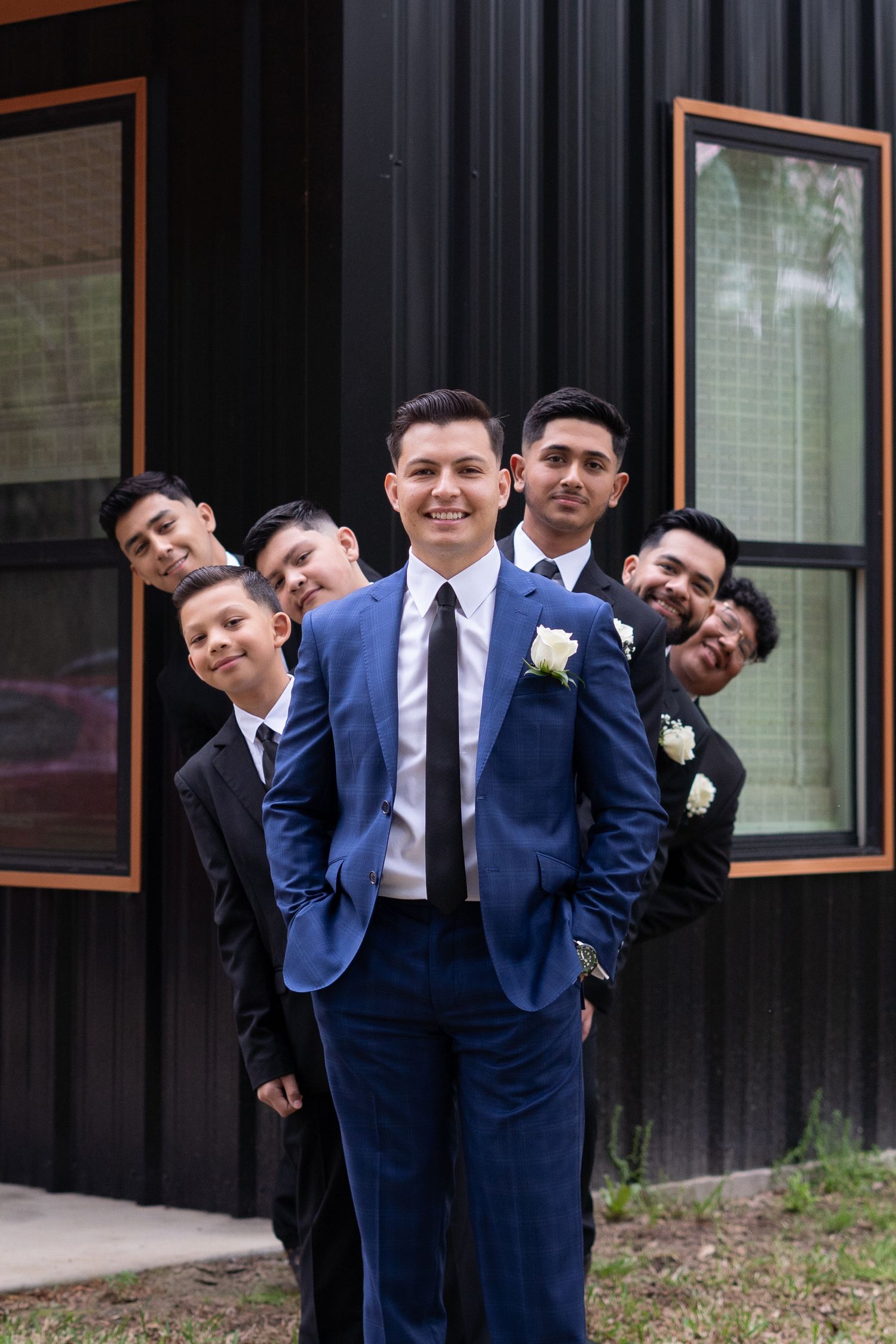 A group in matching navy blue suits pose playfully in a series of connected photos outside a building.