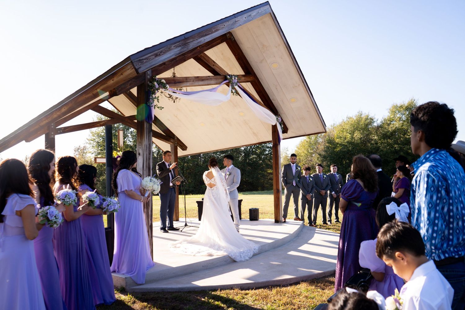 Outdoor wedding ceremony setup with white chairs and floral arrangements under modern architectural venue.