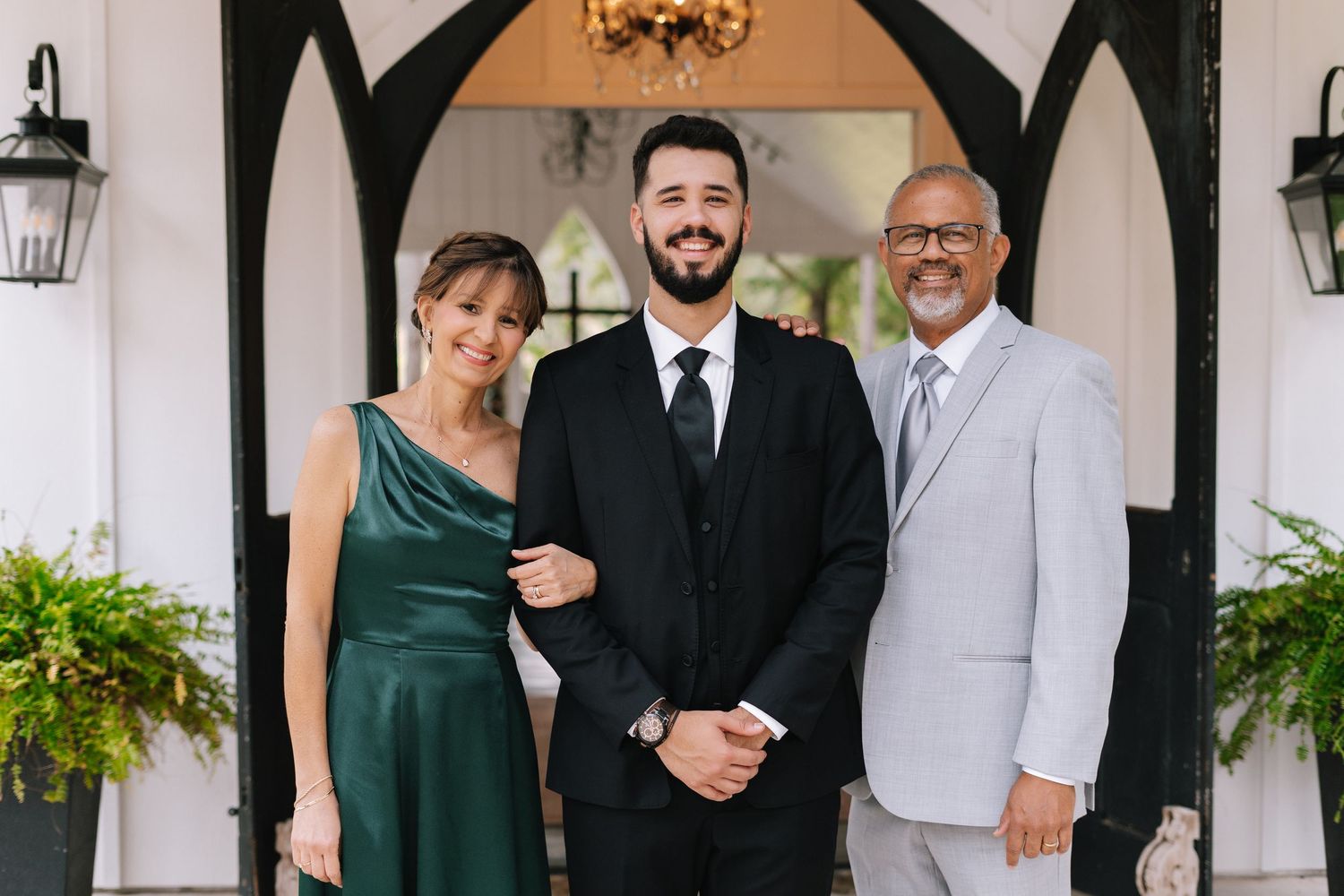 Wedding party poses under white archway with black gothic trim and hanging chandelier.