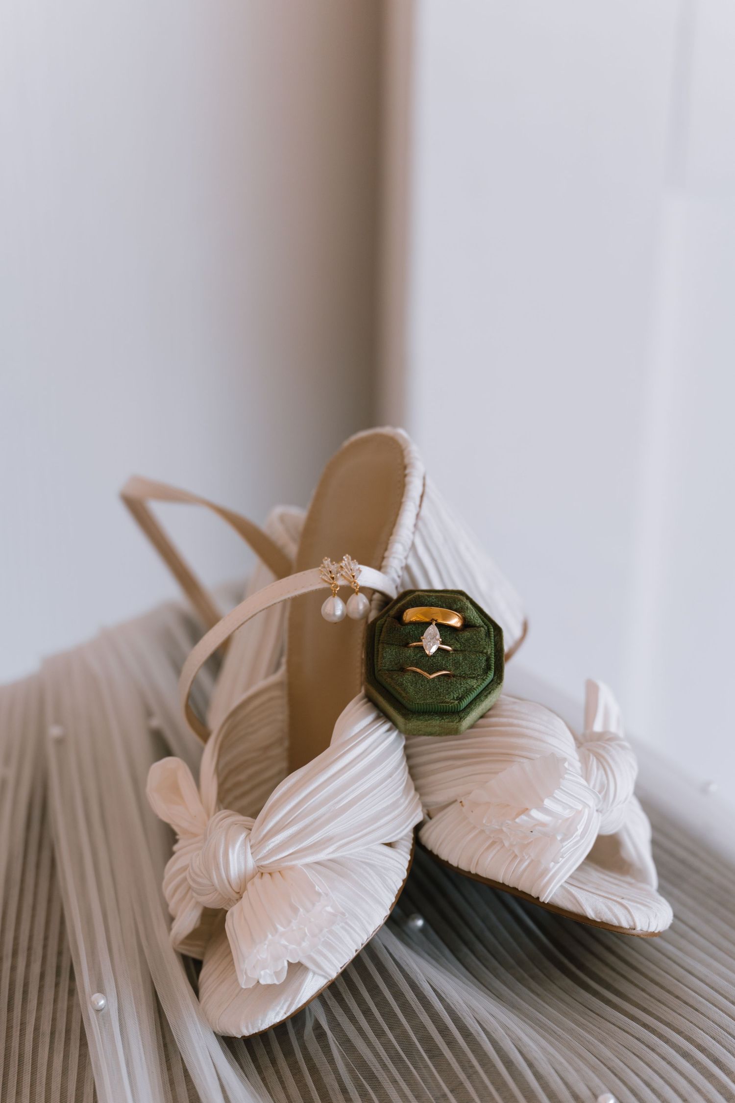 Wedding shoes and jewelry arranged on a wooden surface in soft lighting.
