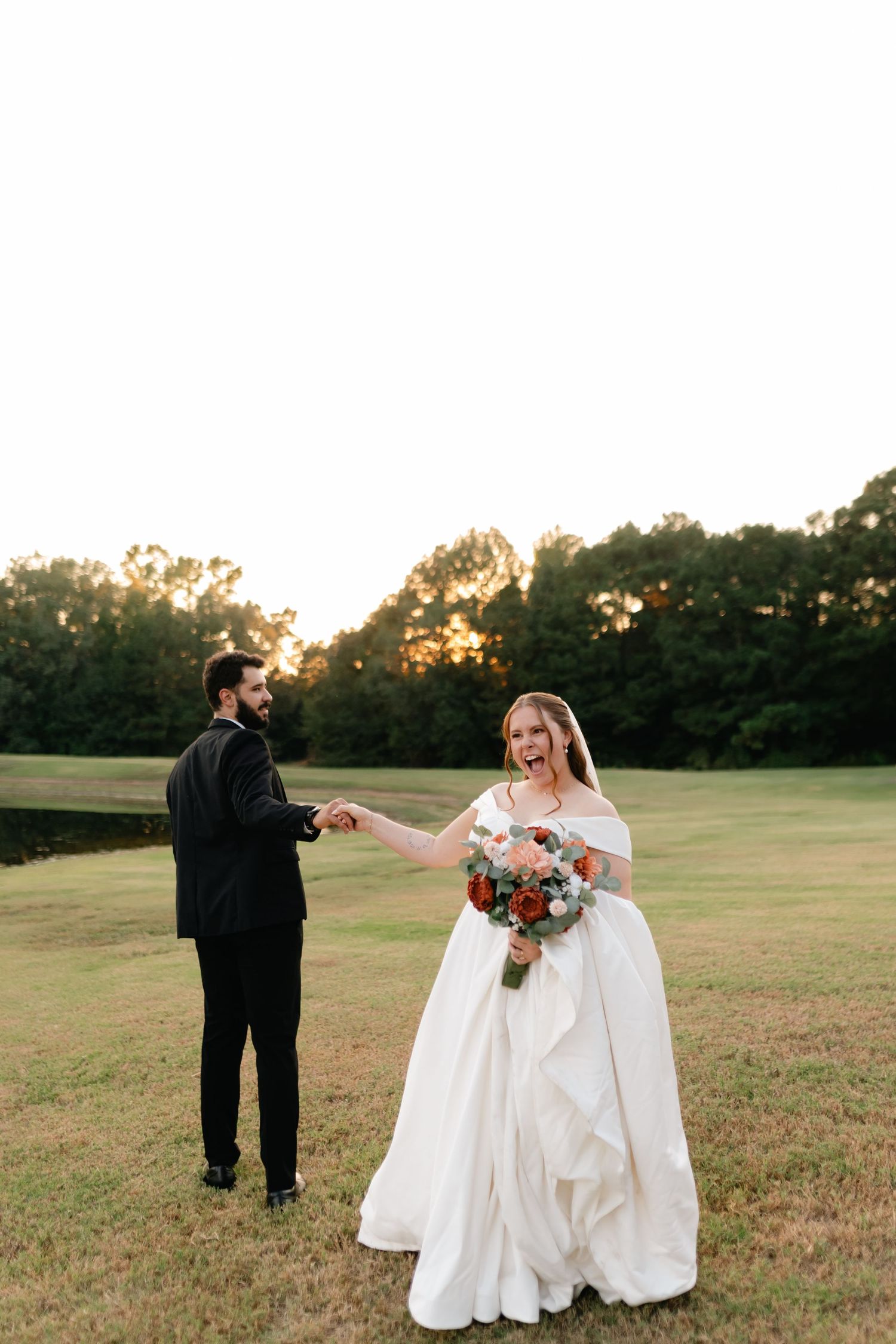 Wedding couple walking through an open field during golden hour with flowing white dress.