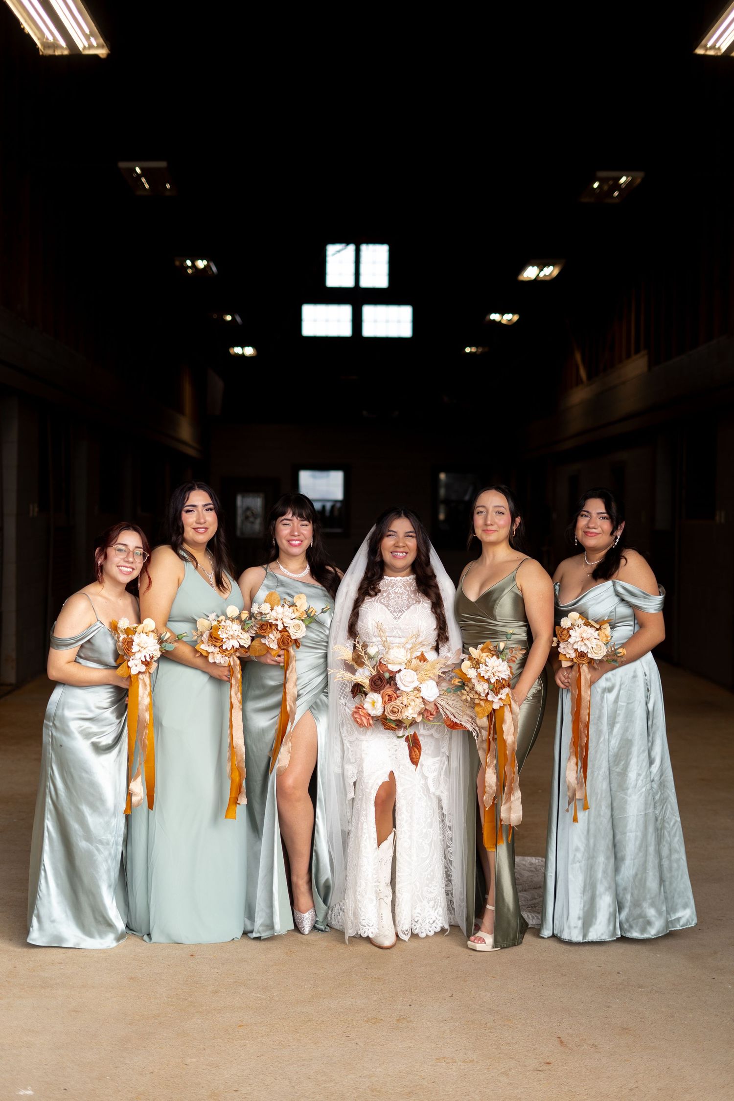 Wedding party in light blue dresses standing in a row holding orange and yellow bouquets at an indoor venue.