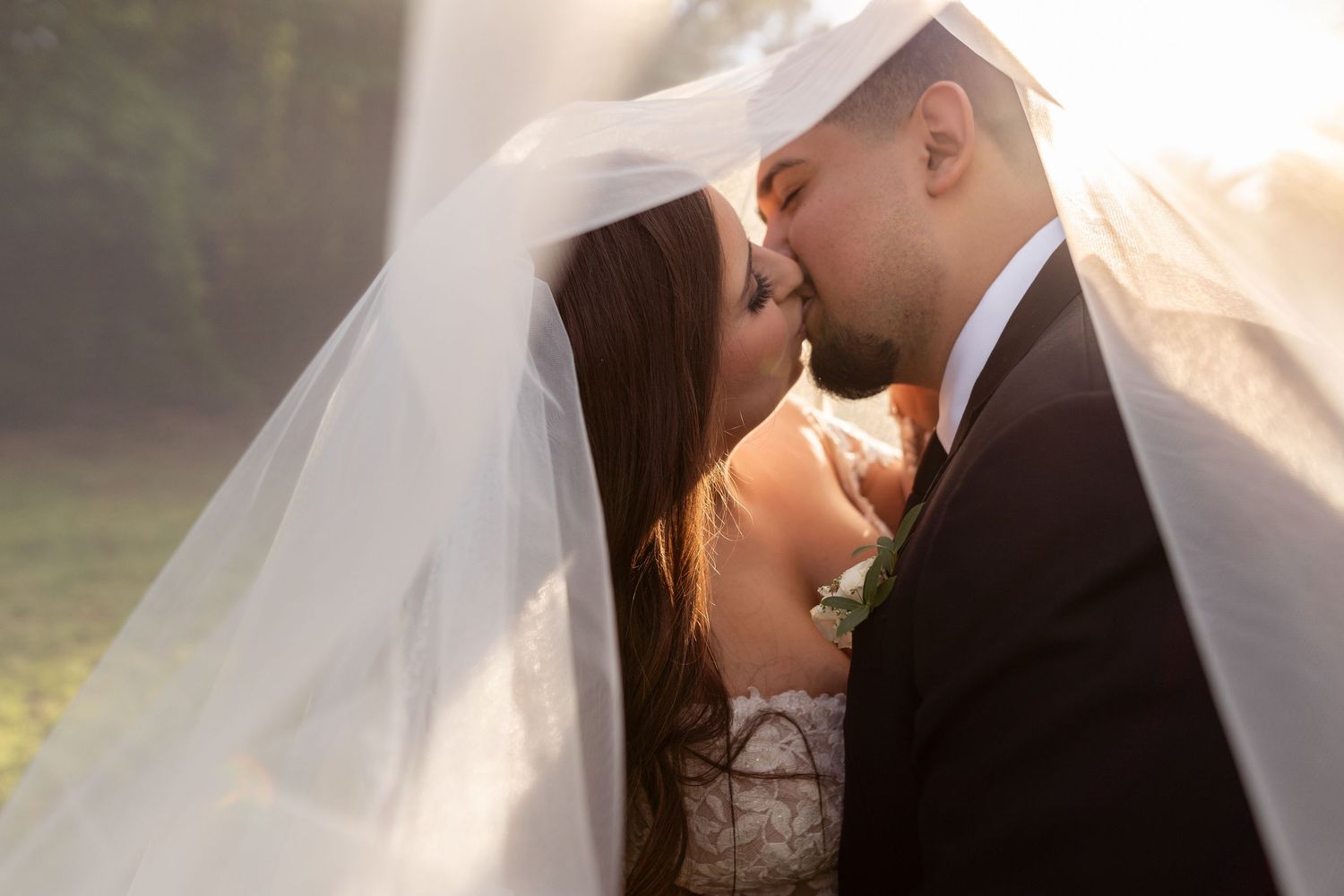 A romantic wedding moment captured under a flowing veil during golden hour lighting.