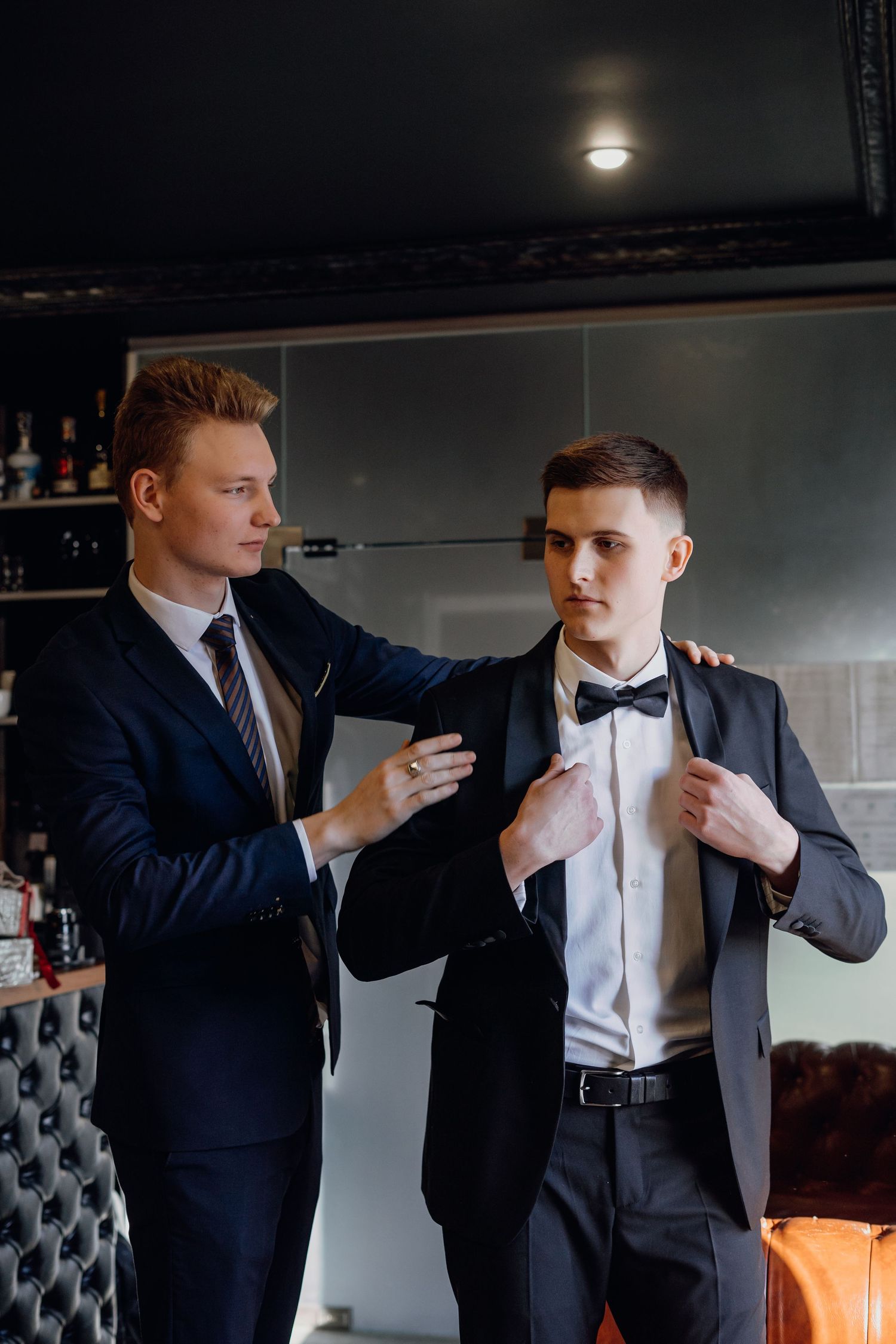 A sequence of four photos showing someone helping another person adjust their bowtie and suit before a formal event.